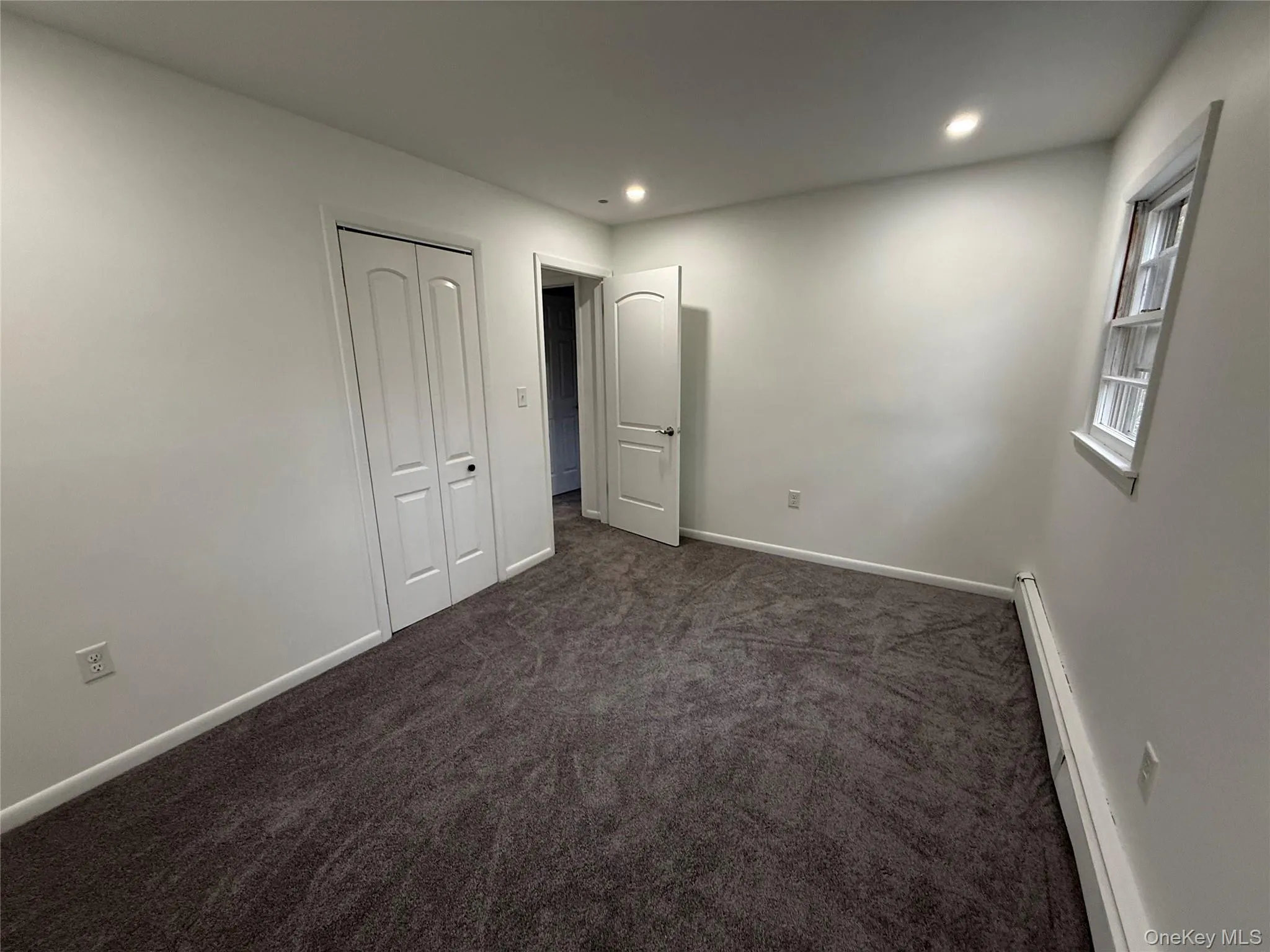 Unfurnished bedroom with baseboard heating, dark carpet, recessed lighting, and a closet Unfurnished bedroom with baseboard heating, dark carpet, recessed lighting, and a closet