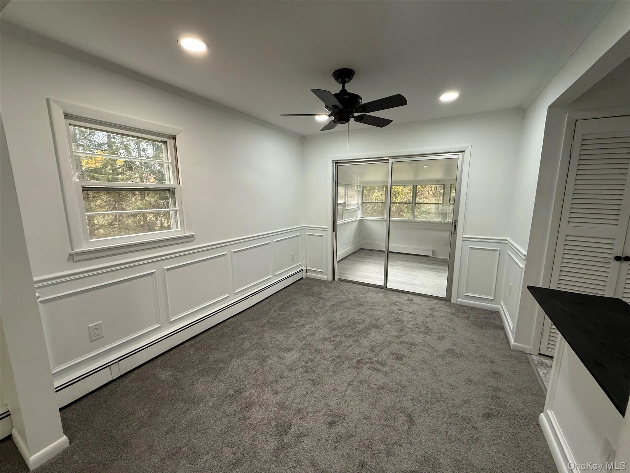 Unfurnished bedroom with baseboard heating, a decorative wall, carpet flooring, a ceiling fan, and wainscoting Unfurnished bedroom with baseboard heating, a decorative wall, carpet flooring, a ceiling fan, and wainscoting