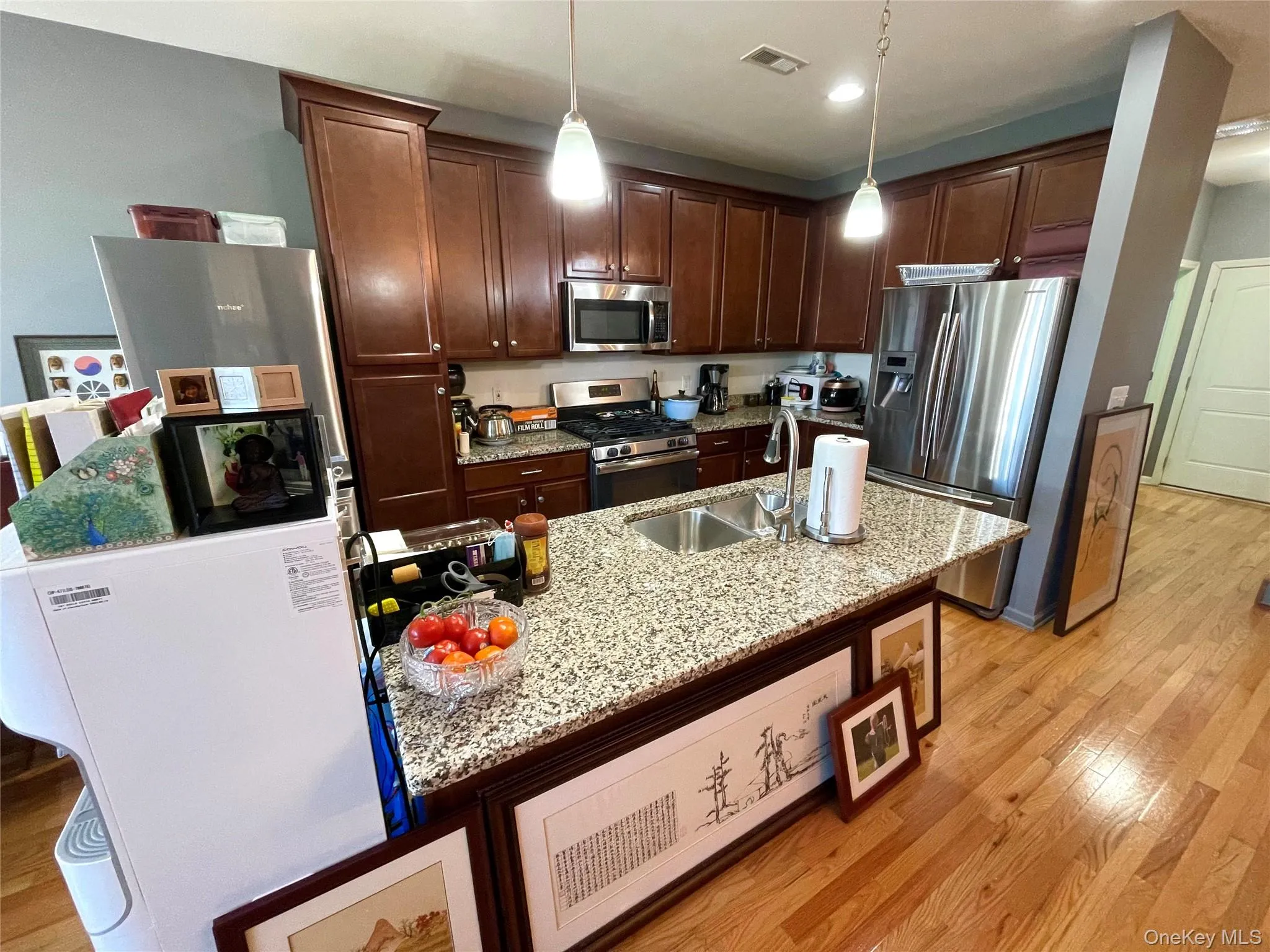 Kitchen with light wood-style floors, appliances with stainless steel finishes, light stone countertops, hanging light fixtures, and recessed lighting Kitchen with light wood-style floors, appliances with stainless steel finishes, light stone countertops, hanging light fixtures, and recessed lighting