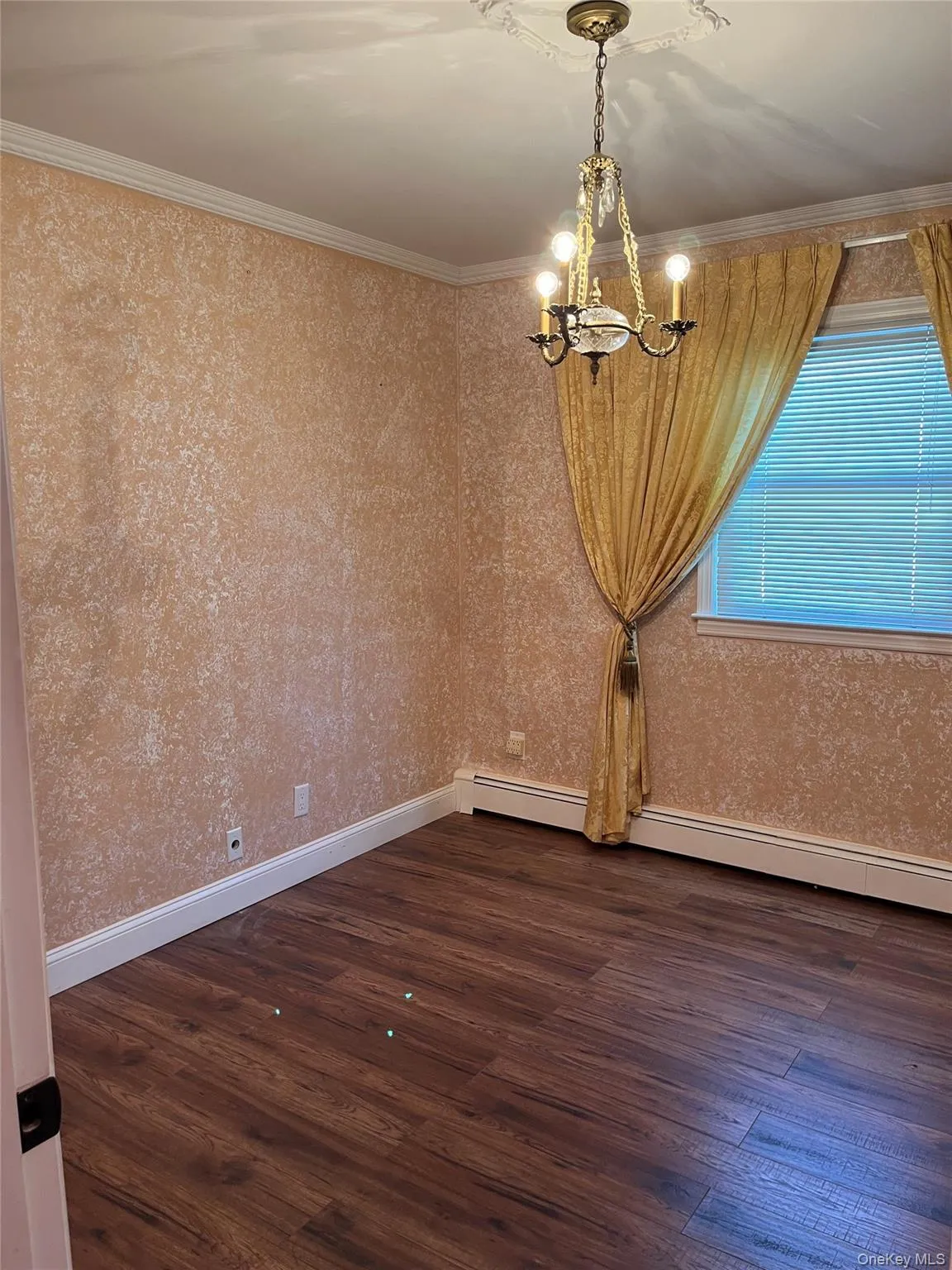 Empty room featuring dark wood-type flooring, a chandelier, crown molding, and a baseboard radiator Empty room featuring dark wood-type flooring, a chandelier, crown molding, and a baseboard radiator