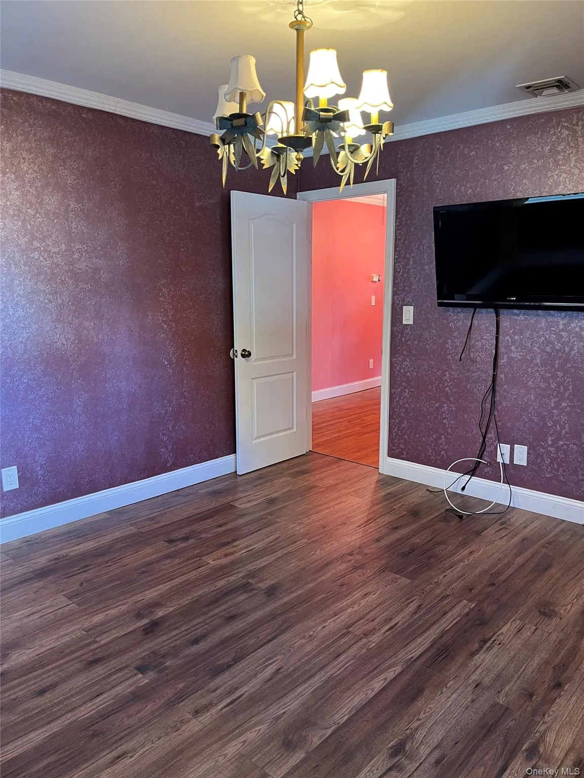 Unfurnished dining area featuring dark wood-style floors, crown molding, a chandelier, and wallpapered walls Unfurnished dining area featuring dark wood-style floors, crown molding, a chandelier, and wallpapered walls
