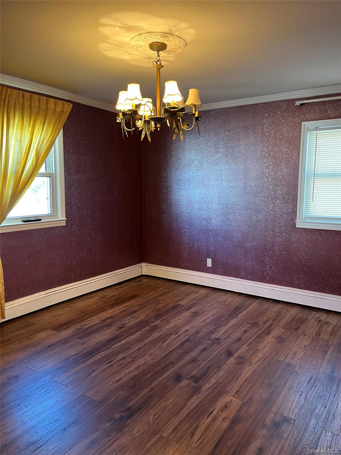 Spare room with dark wood-style floors, ornamental molding, a chandelier, a baseboard radiator, and wallpapered walls Spare room with dark wood-style floors, ornamental molding, a chandelier, a baseboard radiator, and wallpapered walls