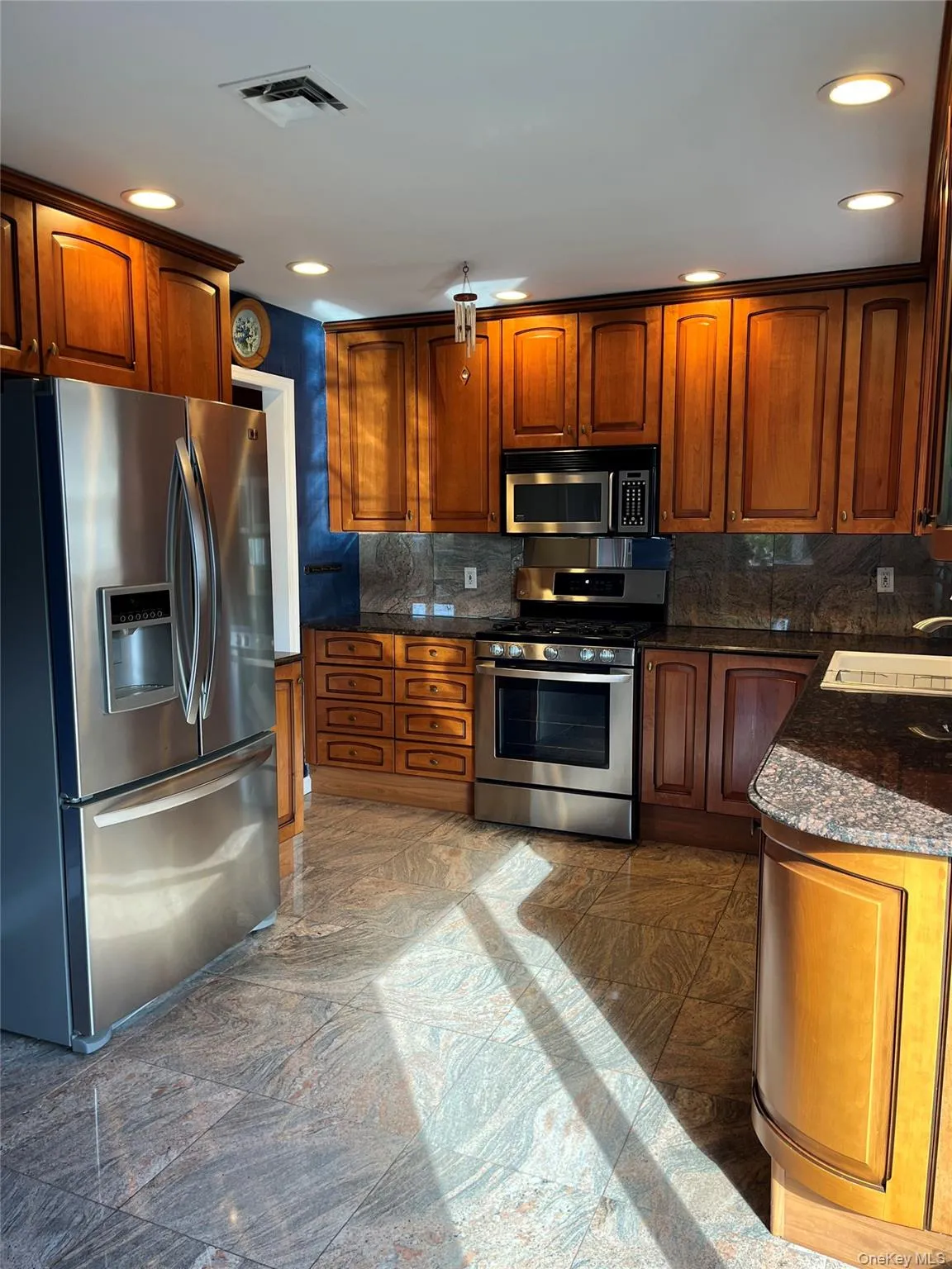 Kitchen with appliances with stainless steel finishes, dark stone counters, brown cabinets, and recessed lighting Kitchen with appliances with stainless steel finishes, dark stone counters, brown cabinets, and recessed lighting