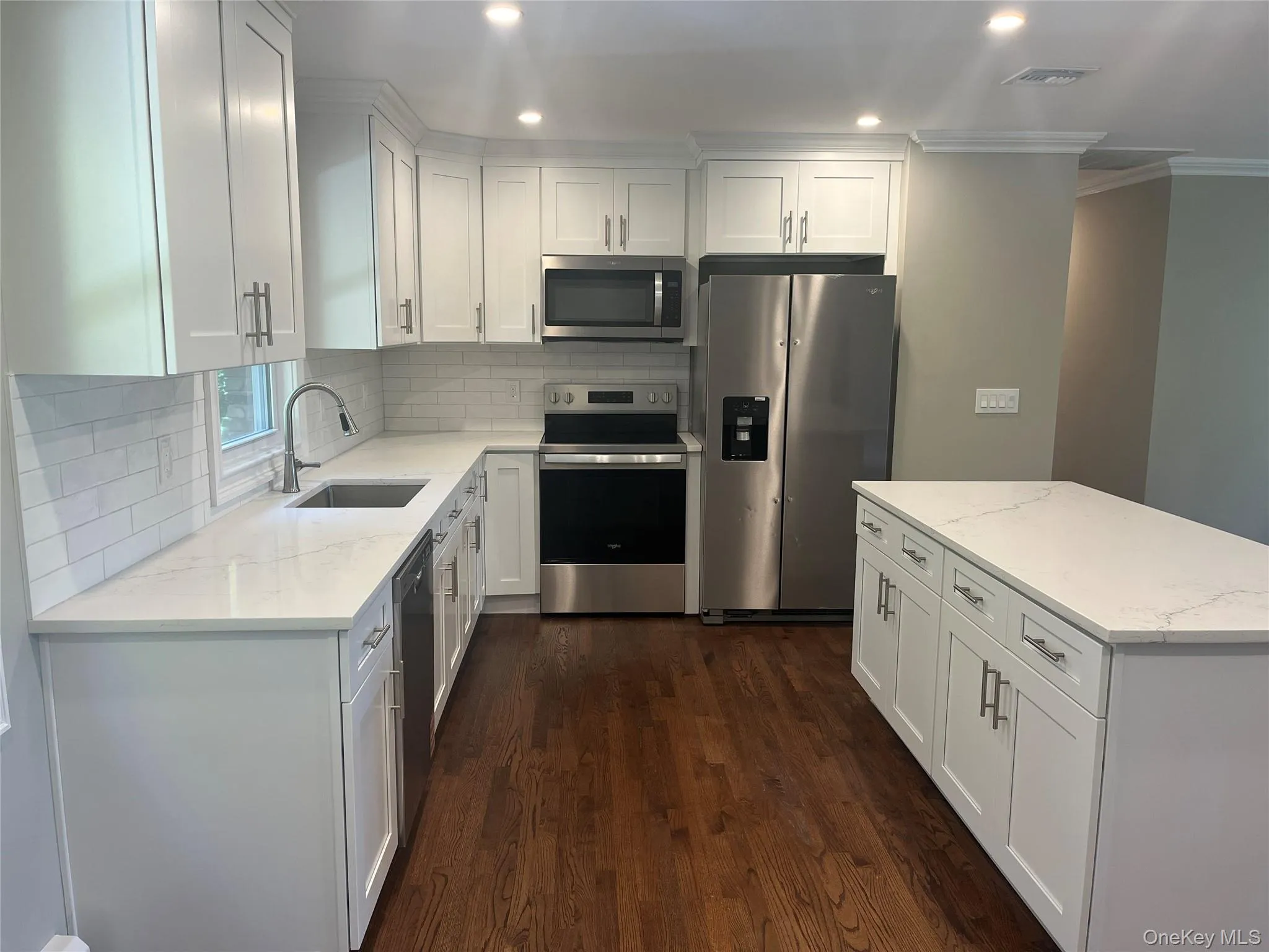 Kitchen featuring white cabinets, stainless steel appliances, light stone counters, dark wood-type flooring, and a center island Kitchen featuring white cabinets, stainless steel appliances, light stone counters, dark wood-type flooring, and a center island