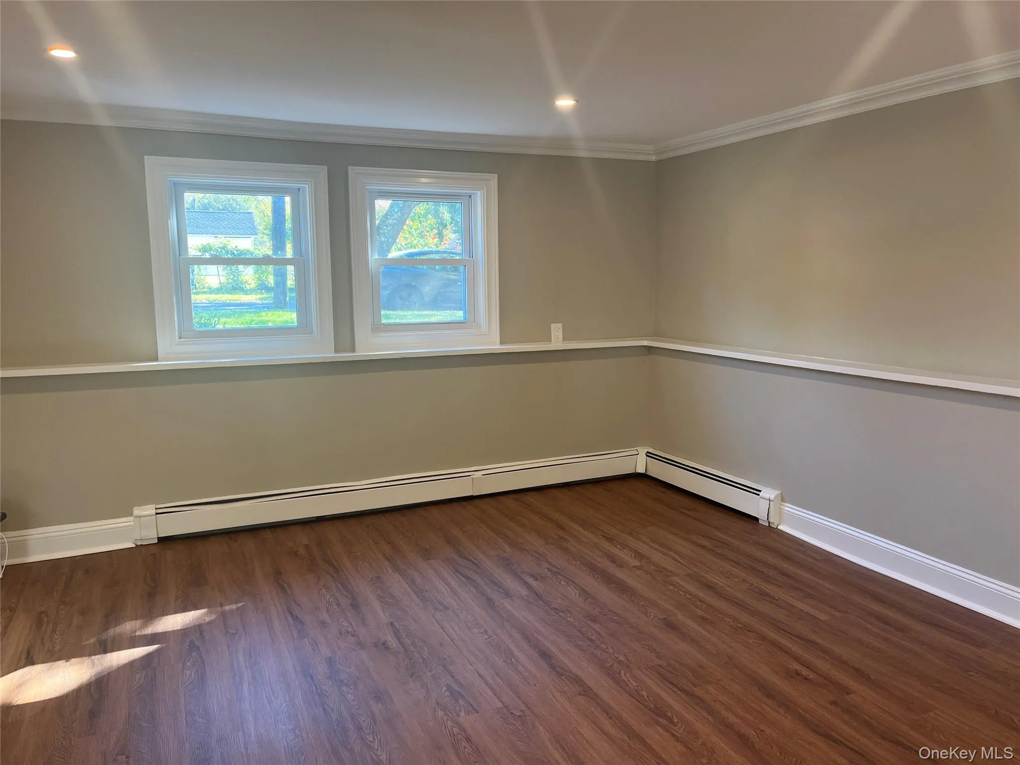 Unfurnished room with dark wood-type flooring, crown molding, recessed lighting, and a baseboard heating unit Unfurnished room with dark wood-type flooring, crown molding, recessed lighting, and a baseboard heating unit