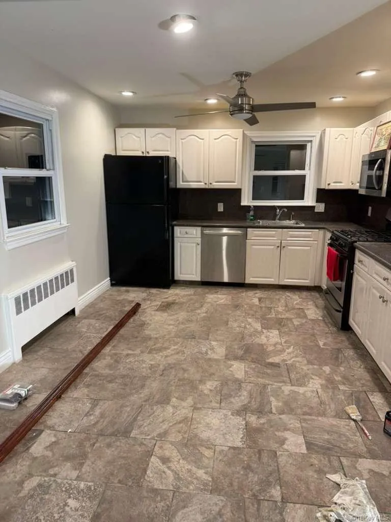 Kitchen with stainless steel appliances, radiator, white cabinets, stone finish floors, and recessed lighting Kitchen with stainless steel appliances, radiator, white cabinets, stone finish floors, and recessed lighting