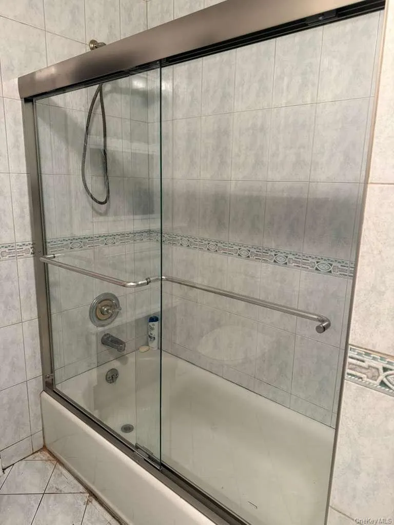 Full bath featuring shower / bath combination with glass door and light tile patterned floors Full bath featuring shower / bath combination with glass door and light tile patterned floors