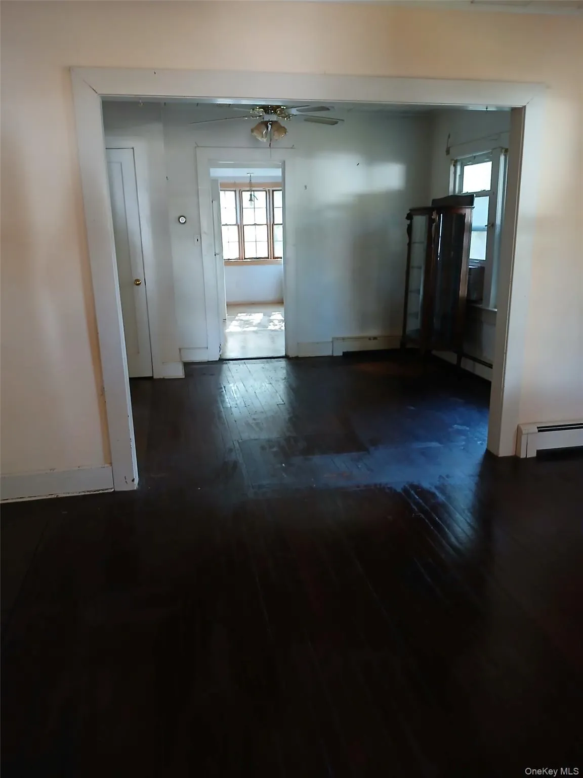 Empty room with dark wood finished floors, ceiling fan, and a baseboard heating unit Empty room with dark wood finished floors, ceiling fan, and a baseboard heating unit