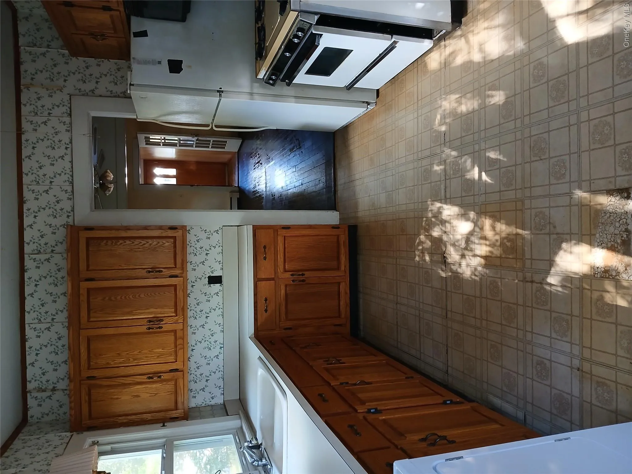 Kitchen featuring brown cabinetry, range, light countertops, wallpapered walls, and fridge Kitchen featuring brown cabinetry, range, light countertops, wallpapered walls, and fridge