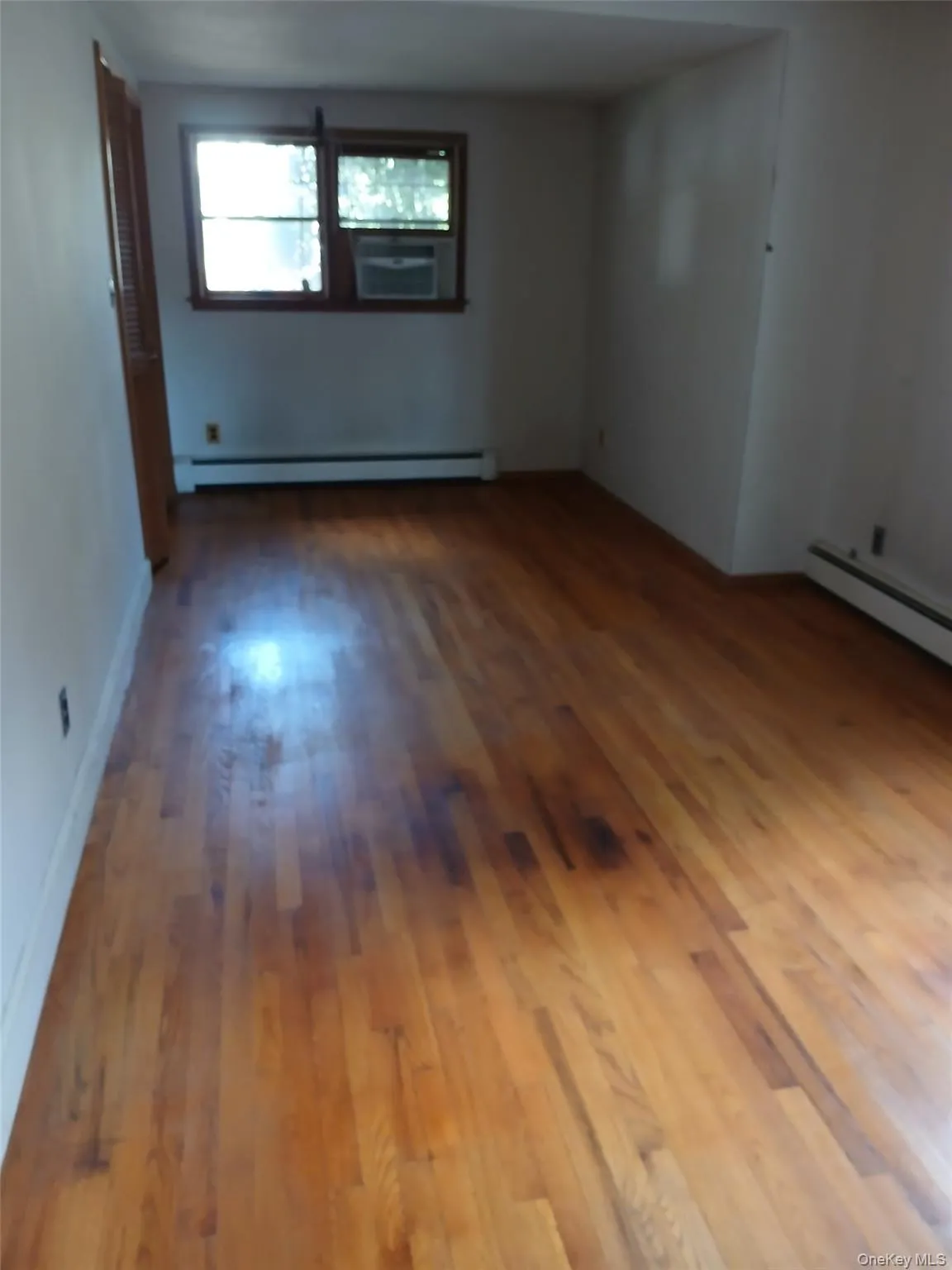 Empty room with hardwood / wood-style floors and baseboard heating Empty room with hardwood / wood-style floors and baseboard heating