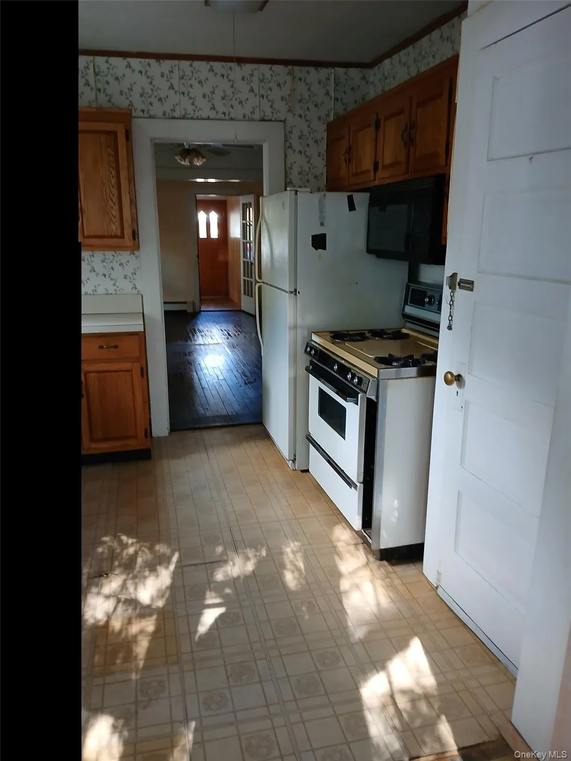 Kitchen featuring white gas range, black microwave, brown cabinets, wallpapered walls, and light countertops Kitchen featuring white gas range, black microwave, brown cabinets, wallpapered walls, and light countertops