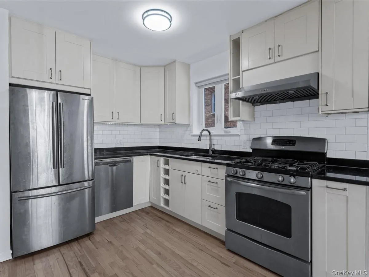 Kitchen with stainless steel appliances, ventilation hood, light wood finished floors, and white cabinetry Kitchen with stainless steel appliances, ventilation hood, light wood finished floors, and white cabinetry