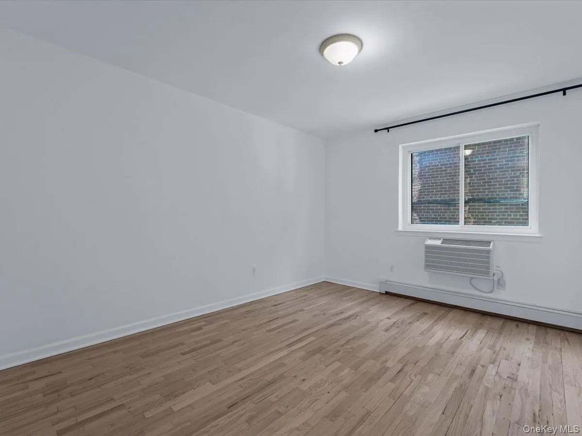 Unfurnished room with light wood-style floors, baseboard heating, and a wall mounted AC Unfurnished room with light wood-style floors, baseboard heating, and a wall mounted AC