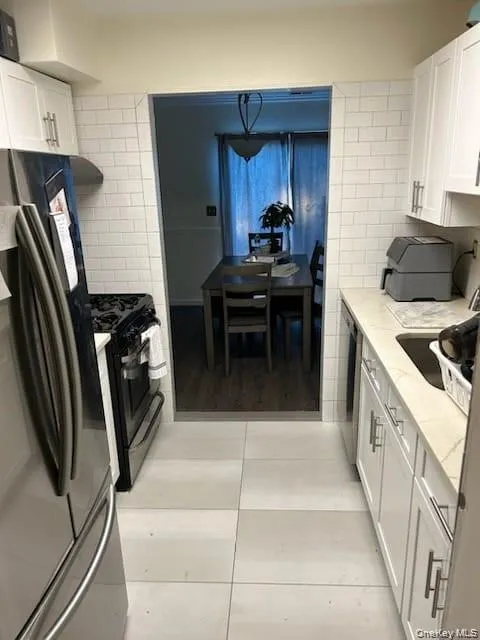 Kitchen featuring white cabinets, stainless steel appliances, light tile patterned floors, backsplash, and tile walls Kitchen featuring white cabinets, stainless steel appliances, light tile patterned floors, backsplash, and tile walls