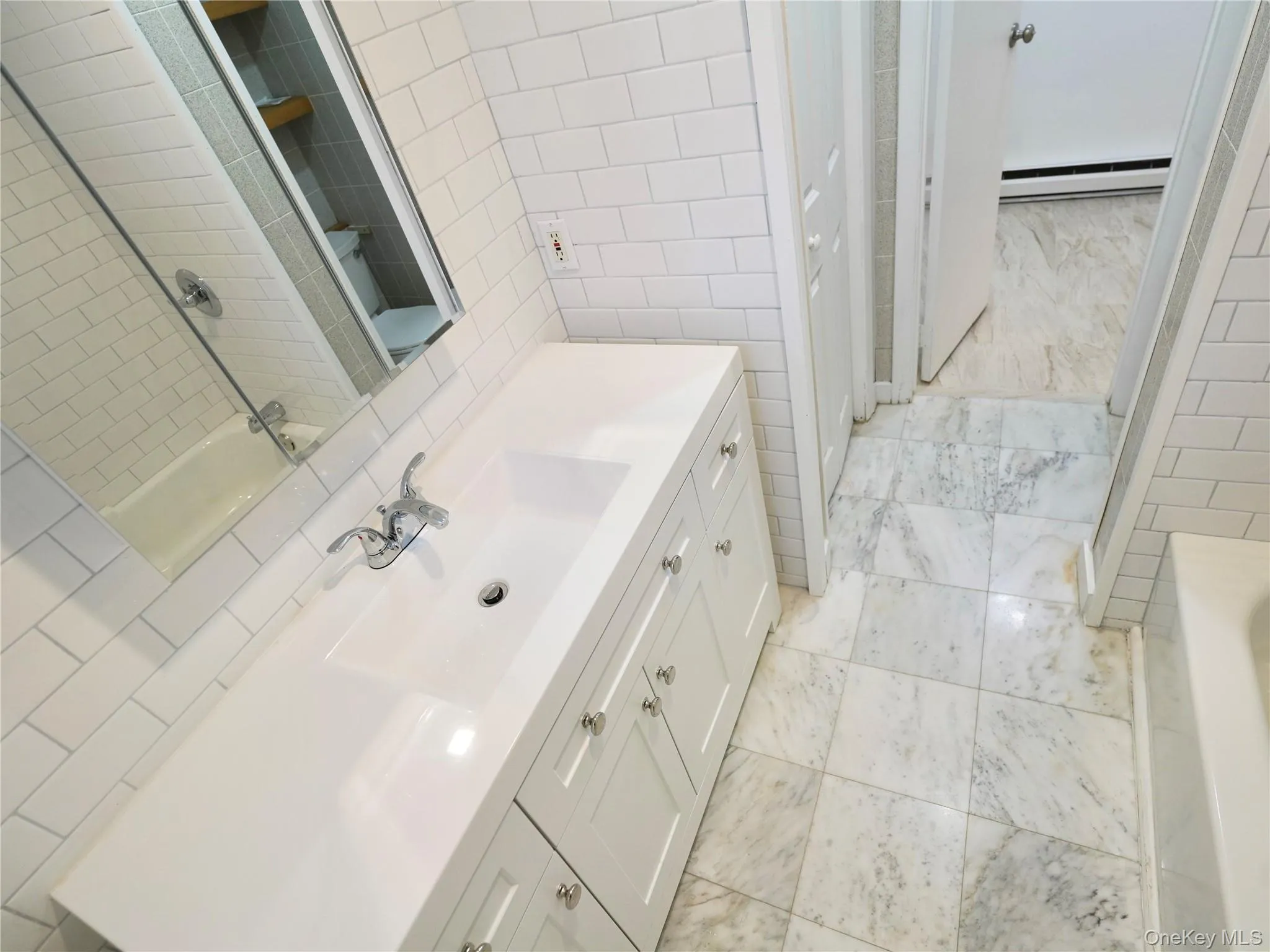 Full bath featuring vanity, tile walls, shower / bath combination, light tile patterned flooring, and a baseboard radiator Full bath featuring vanity, tile walls, shower / bath combination, light tile patterned flooring, and a baseboard radiator