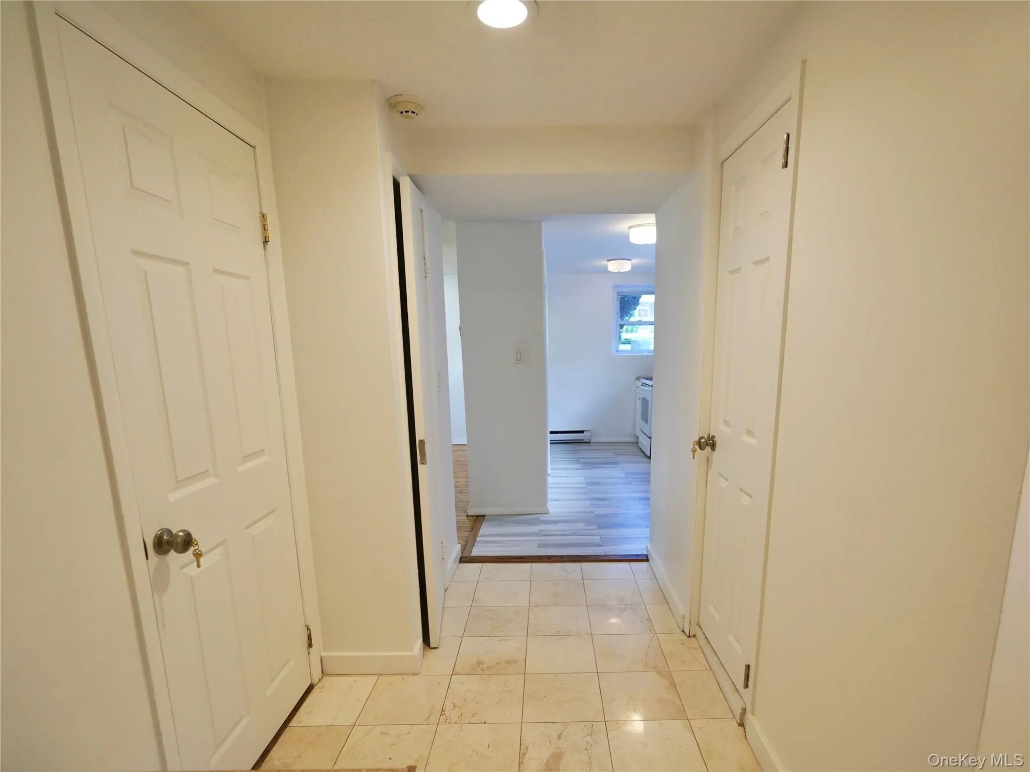 Corridor featuring light tile patterned floors and a baseboard heating unit Corridor featuring light tile patterned floors and a baseboard heating unit