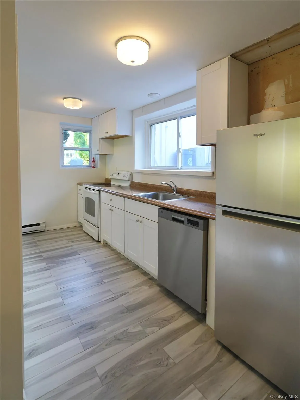 Kitchen with appliances with stainless steel finishes, white cabinets, light wood-style floors, and baseboard heating Kitchen with appliances with stainless steel finishes, white cabinets, light wood-style floors, and baseboard heating