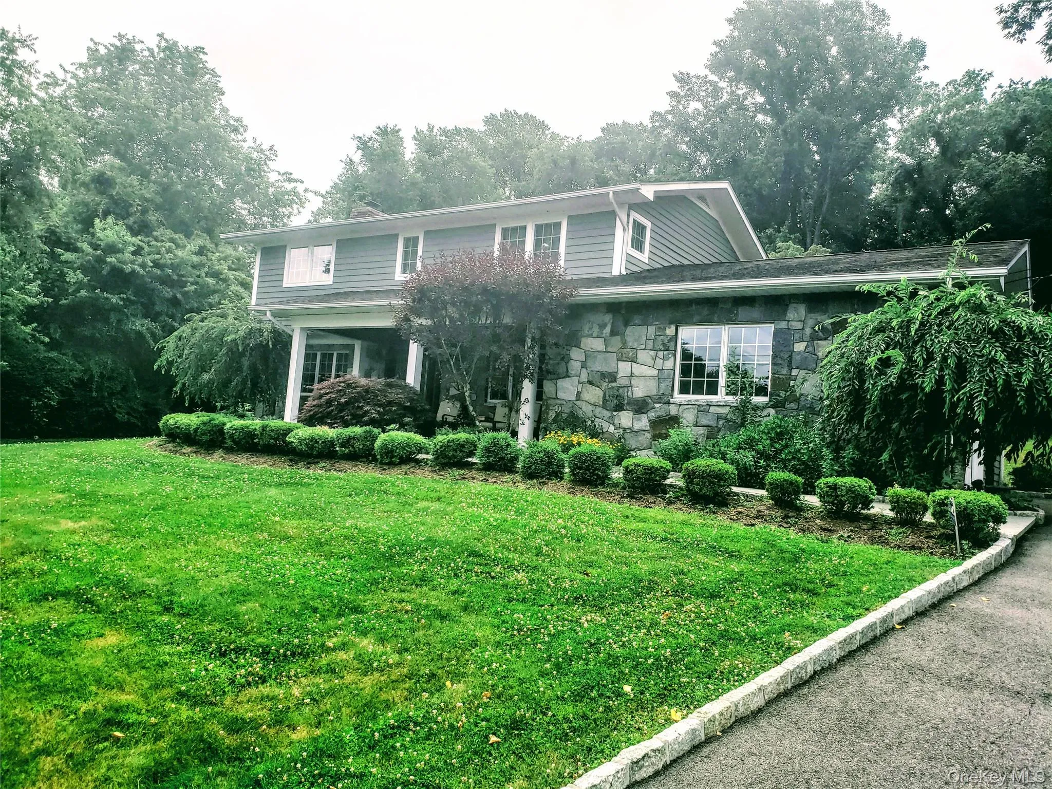 View of front of property with stone siding, a front yard, a porch, and view of scattered trees View of front of property with stone siding, a front yard, a porch, and view of scattered trees
