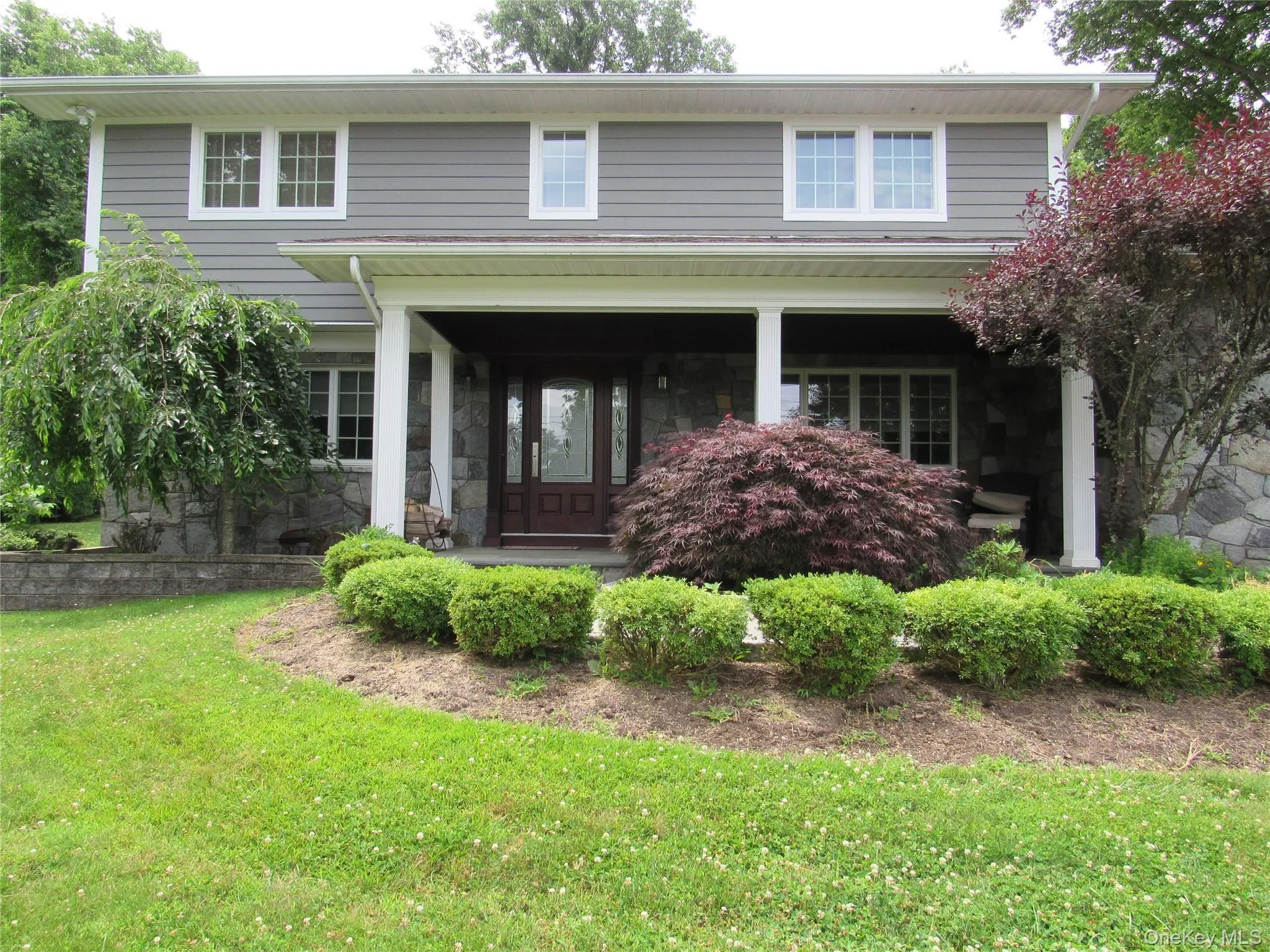 View of front of home with covered porch, a front lawn, and stone siding View of front of home with covered porch, a front lawn, and stone siding