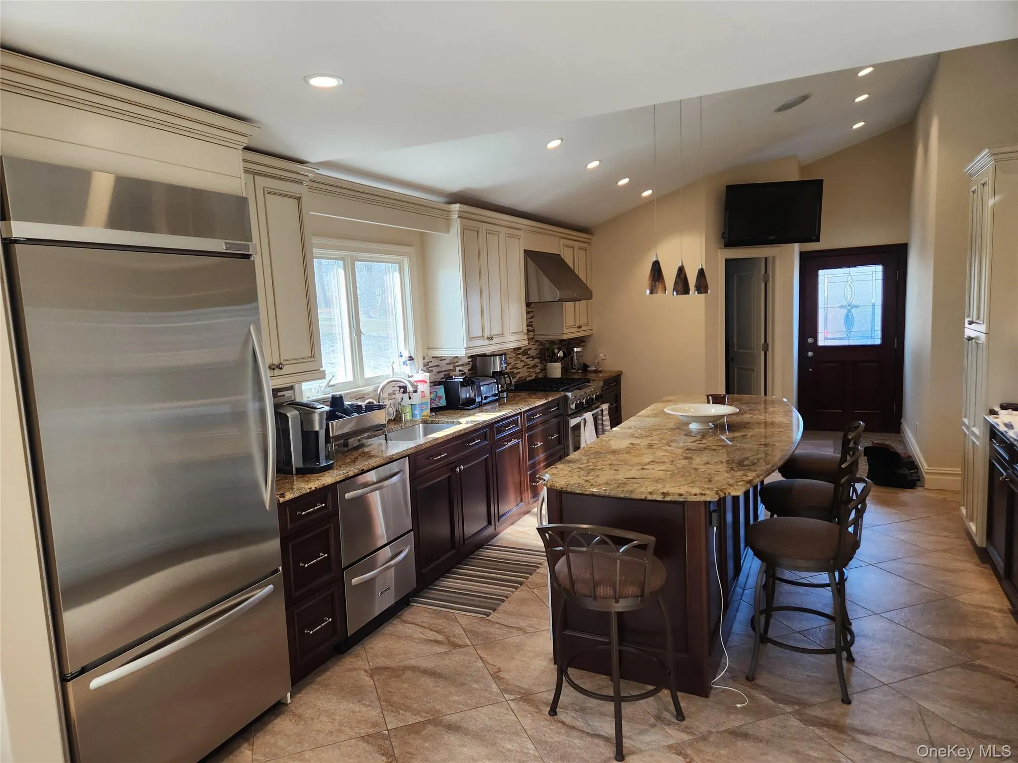 Kitchen with cream cabinets, stainless steel appliances, a breakfast bar, light stone countertops, and dark brown cabinetry Kitchen with cream cabinets, stainless steel appliances, a breakfast bar, light stone countertops, and dark brown cabinetry