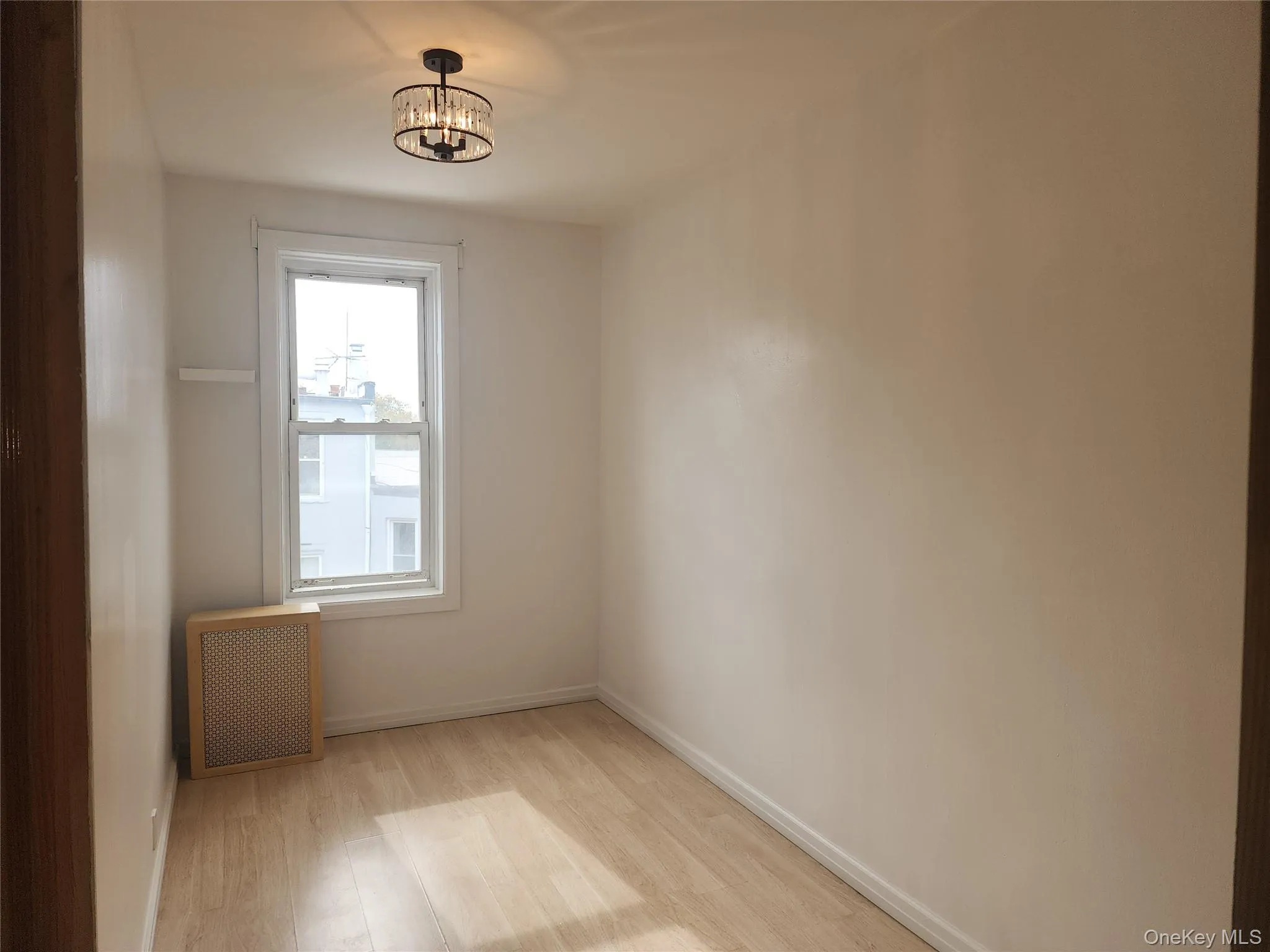 Spare room featuring light wood-style floors, radiator, and a chandelier Spare room featuring light wood-style floors, radiator, and a chandelier