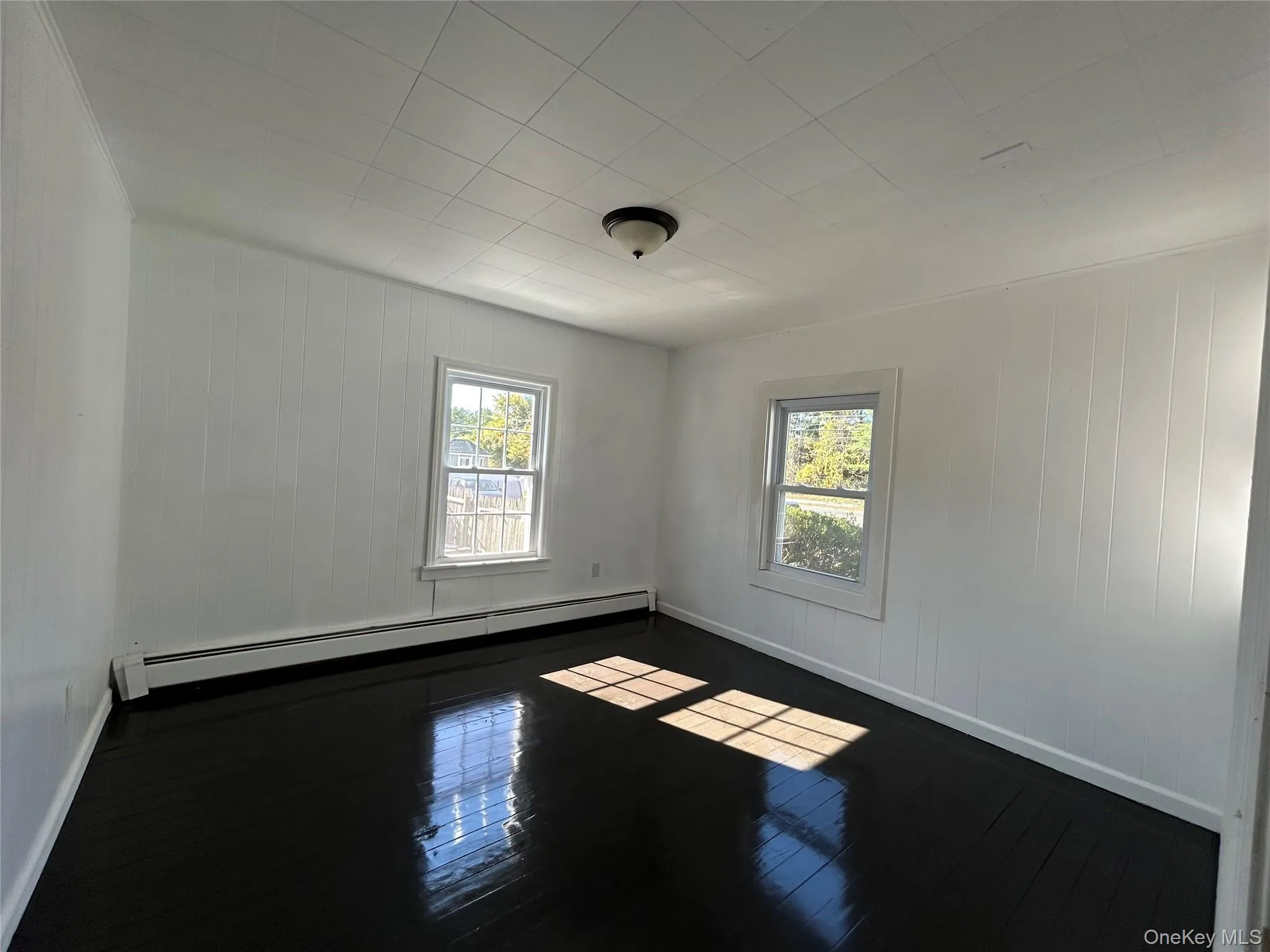 Unfurnished room with healthy amount of natural light, dark wood finished floors, baseboard heating, and wooden walls Unfurnished room with healthy amount of natural light, dark wood finished floors, baseboard heating, and wooden walls