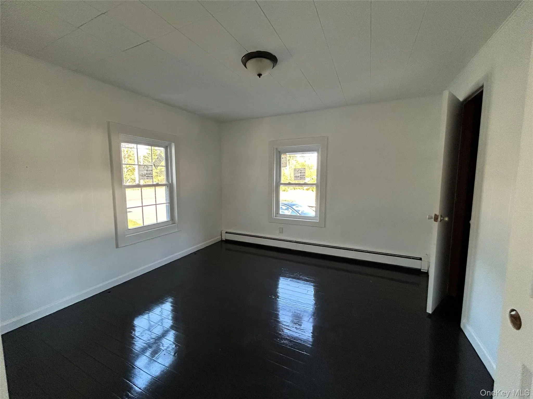 Unfurnished room with baseboard heating, dark wood-type flooring, and plenty of natural light Unfurnished room with baseboard heating, dark wood-type flooring, and plenty of natural light