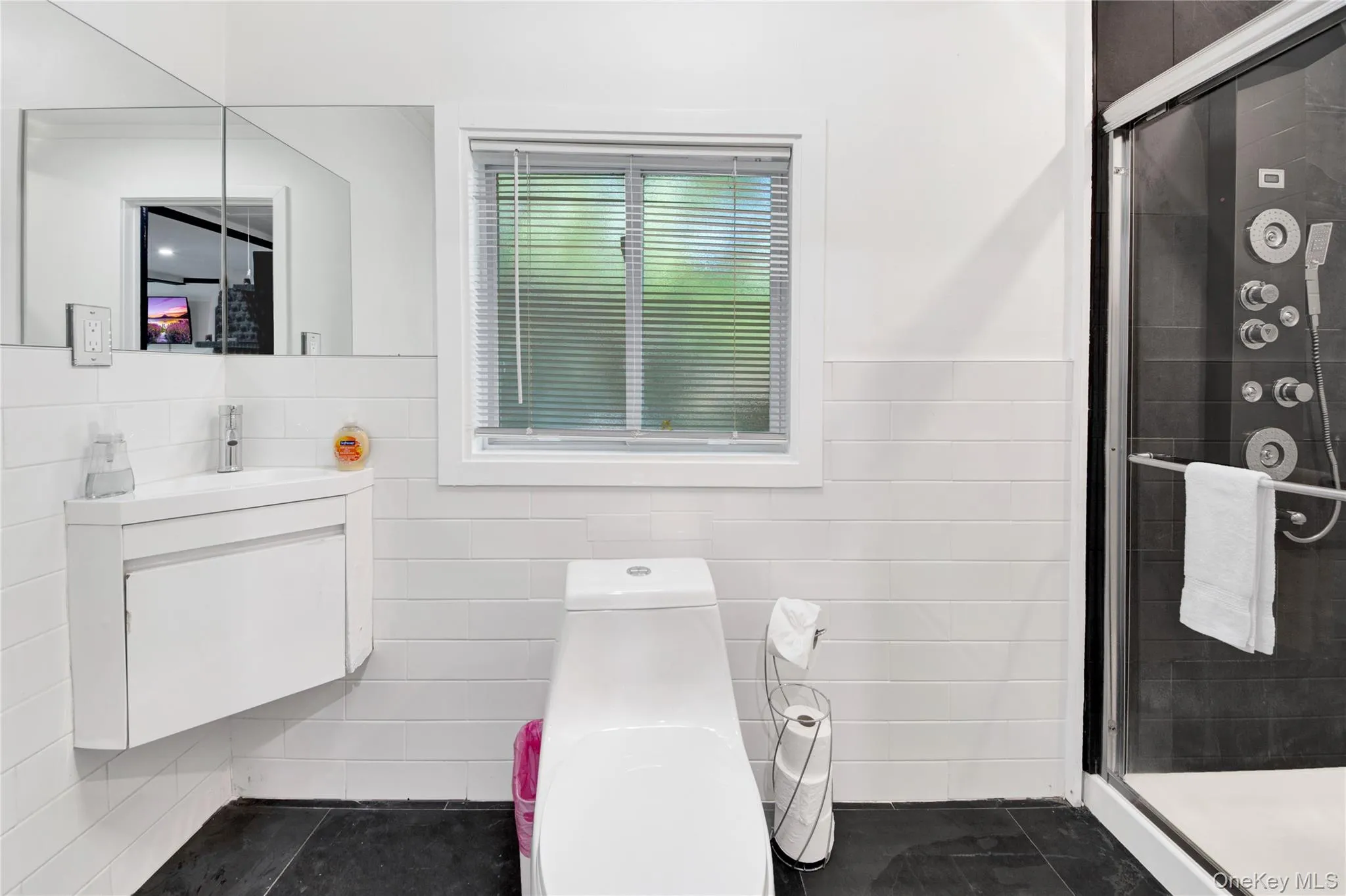 Bathroom with tile walls, vanity, a shower stall, a wainscoted wall, and dark tile patterned floors Bathroom with tile walls, vanity, a shower stall, a wainscoted wall, and dark tile patterned floors
