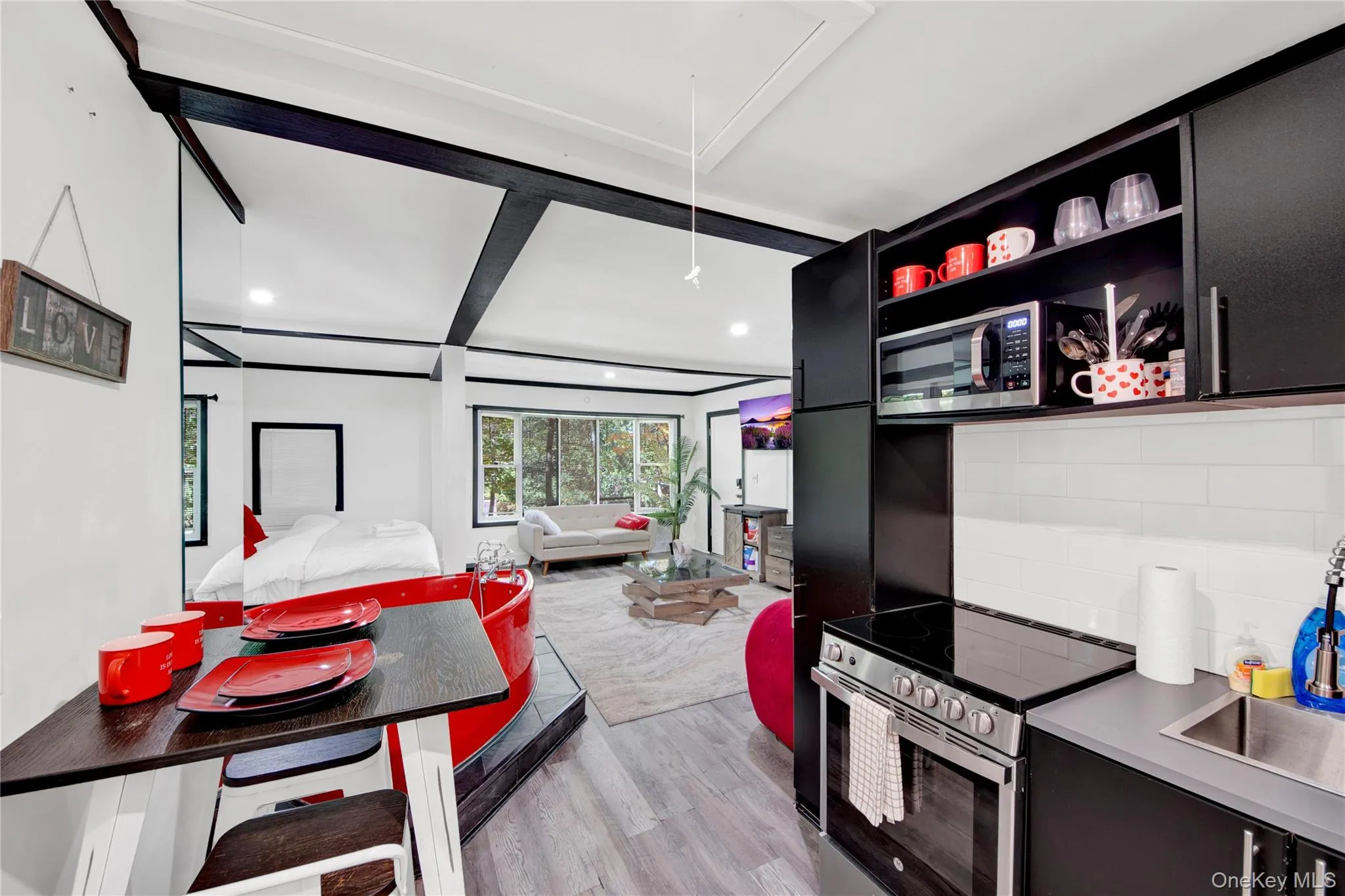 Kitchen featuring stainless steel appliances, dark cabinetry, light wood-style floors, beamed ceiling, and recessed lighting Kitchen featuring stainless steel appliances, dark cabinetry, light wood-style floors, beamed ceiling, and recessed lighting
