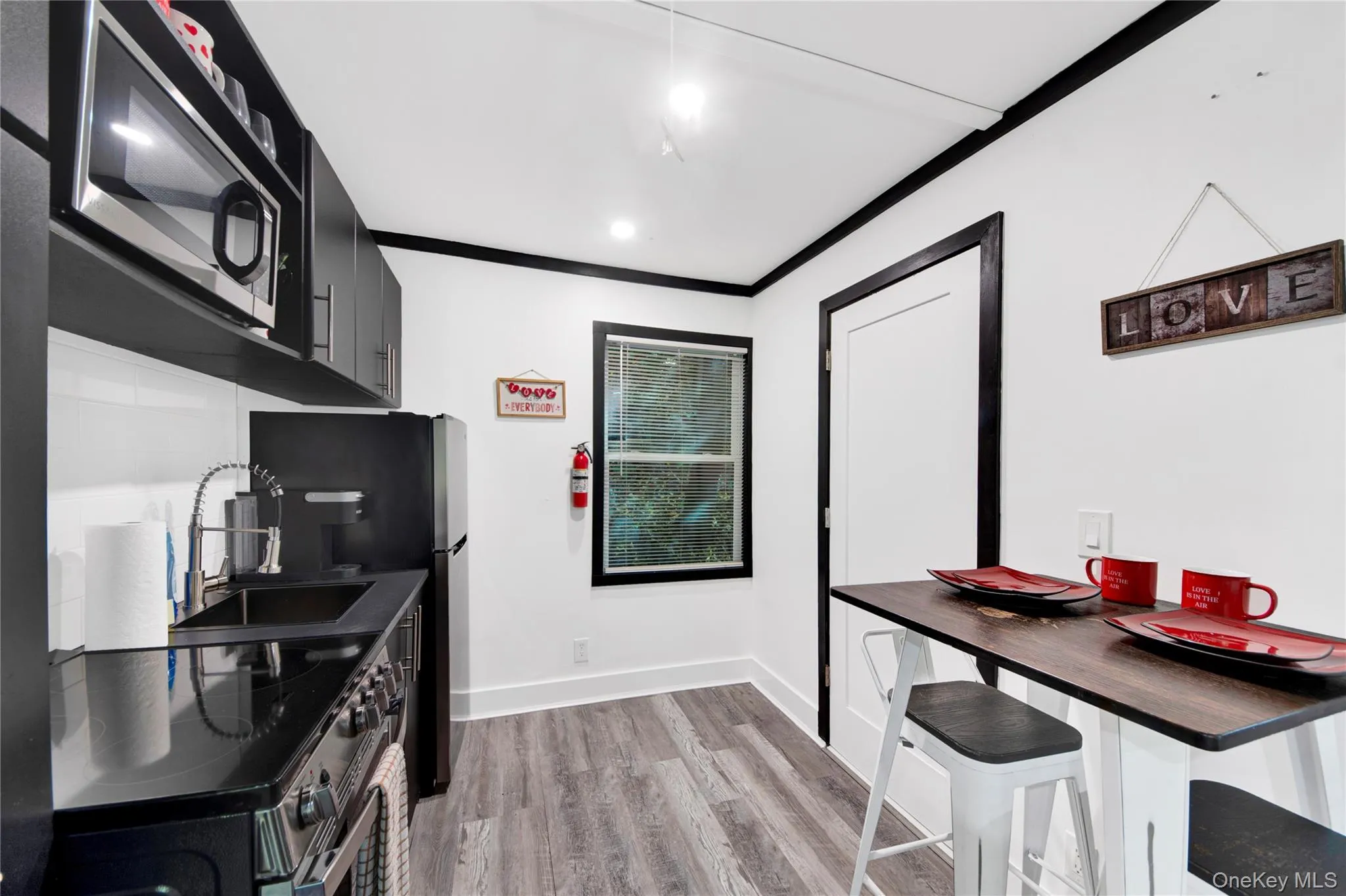 Kitchen featuring dark cabinetry, dark countertops, stainless steel appliances, light wood-style flooring, and ornamental molding Kitchen featuring dark cabinetry, dark countertops, stainless steel appliances, light wood-style flooring, and ornamental molding