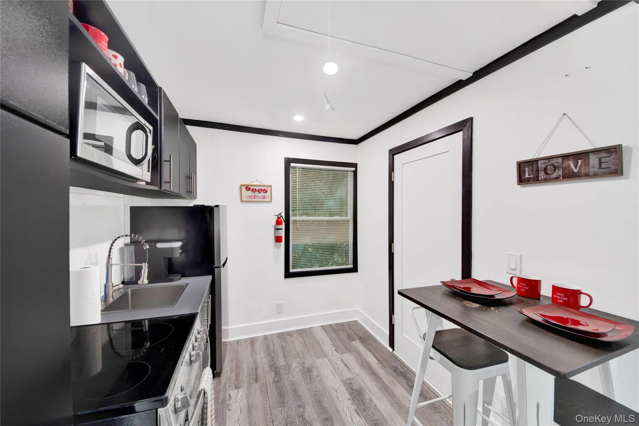 Kitchen featuring light wood finished floors, appliances with stainless steel finishes, recessed lighting, ornamental molding, and dark cabinets Kitchen featuring light wood finished floors, appliances with stainless steel finishes, recessed lighting, ornamental molding, and dark cabinets