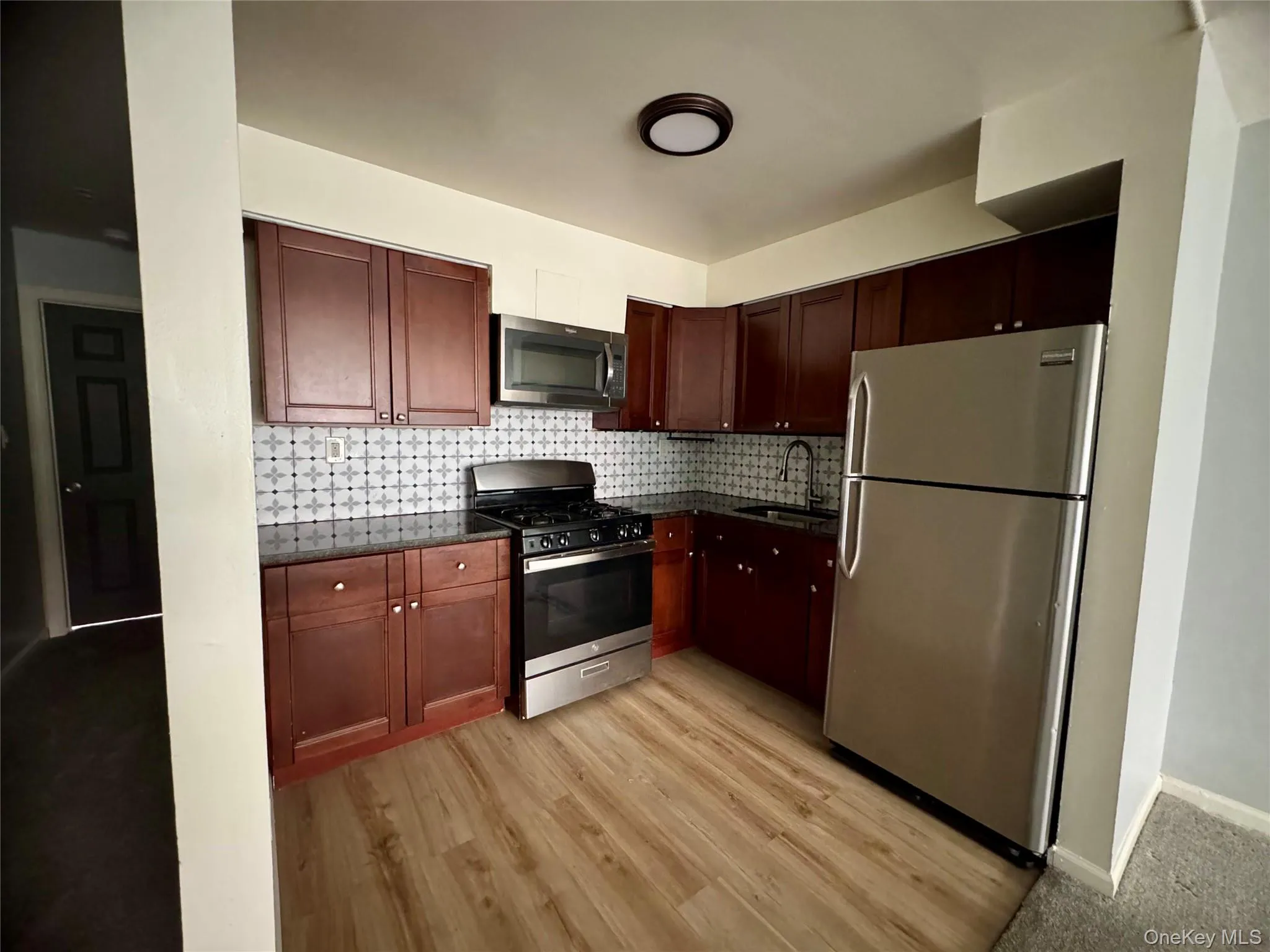 Kitchen with stainless steel appliances, tasteful backsplash, dark stone counters, and light wood finished floors Kitchen with stainless steel appliances, tasteful backsplash, dark stone counters, and light wood finished floors