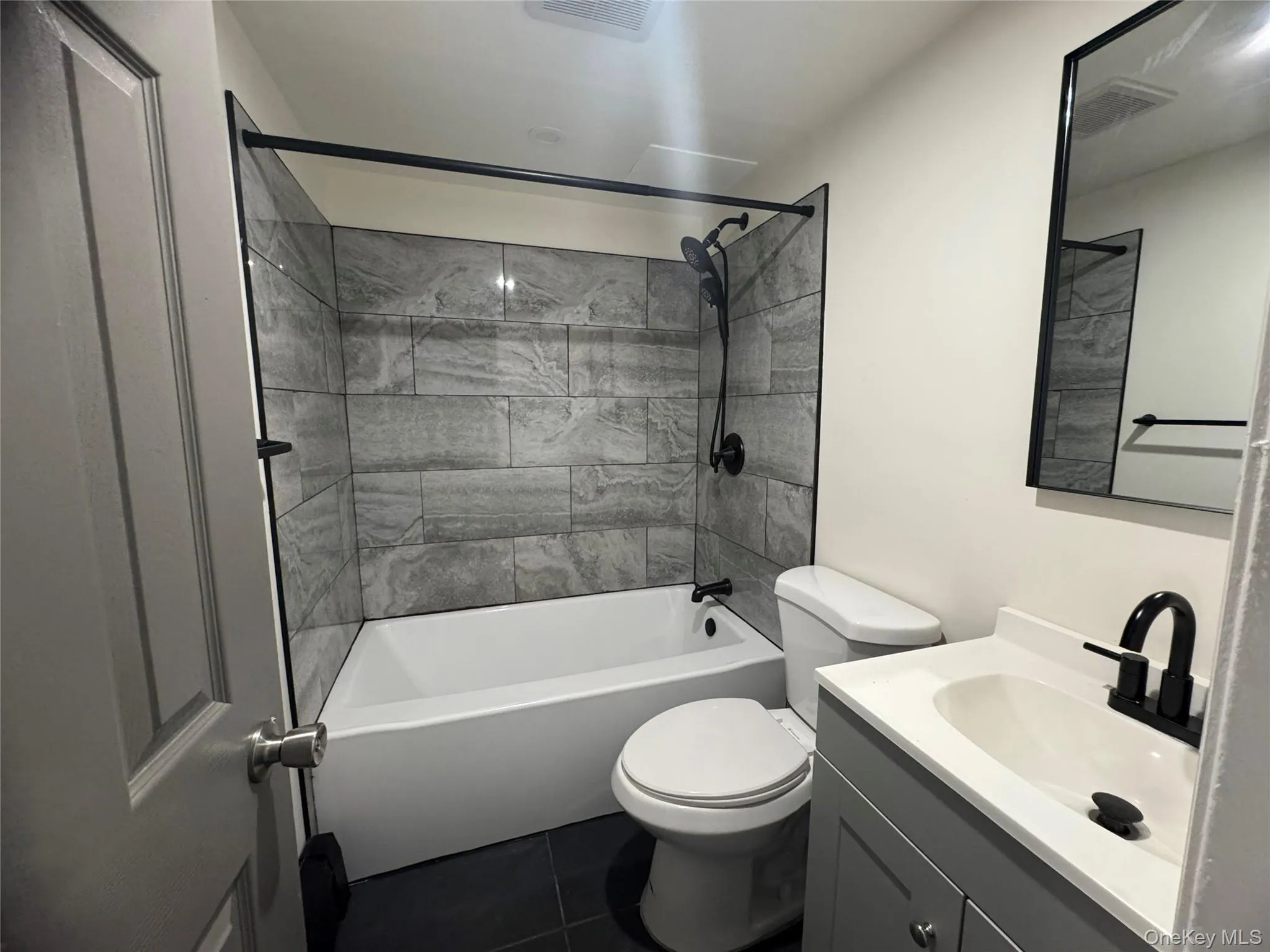 Bathroom featuring bathing tub / shower combination, vanity, and dark tile patterned flooring Bathroom featuring bathing tub / shower combination, vanity, and dark tile patterned flooring