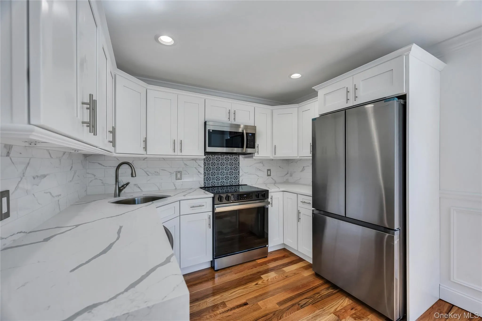 Kitchen featuring stainless steel appliances, light stone counters, white cabinets, dark wood-style floors, and backsplash Kitchen featuring stainless steel appliances, light stone counters, white cabinets, dark wood-style floors, and backsplash