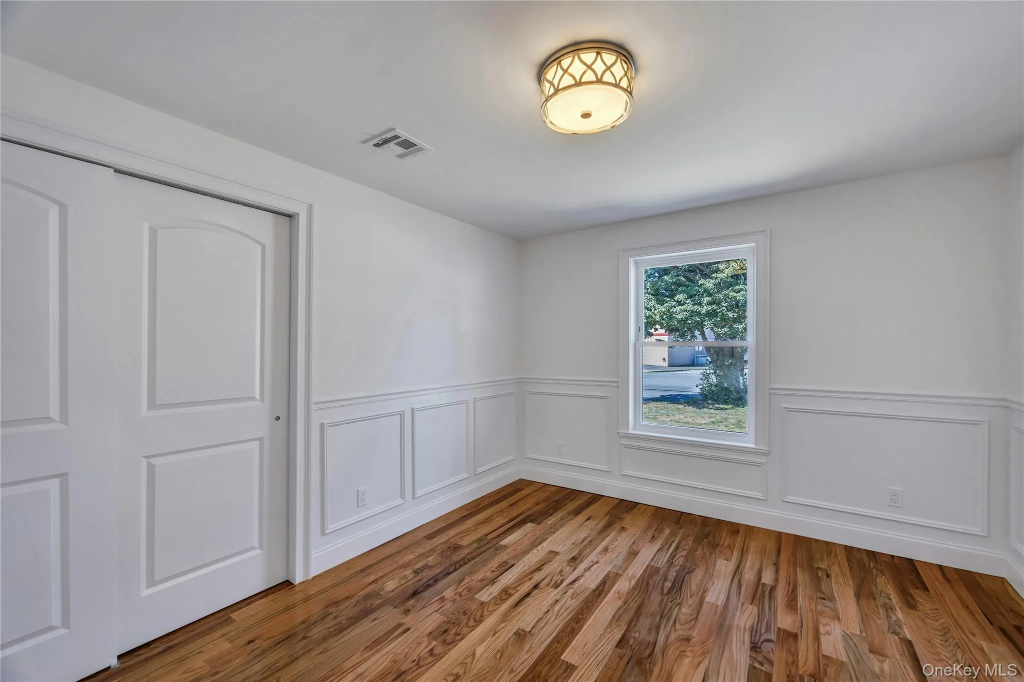 Spare room featuring wood finished floors, a decorative wall, and a wainscoted wall Spare room featuring wood finished floors, a decorative wall, and a wainscoted wall