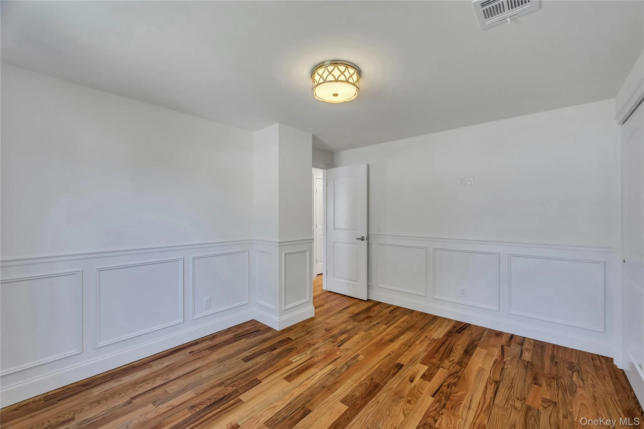 Spare room featuring wood finished floors, wainscoting, and a decorative wall Spare room featuring wood finished floors, wainscoting, and a decorative wall