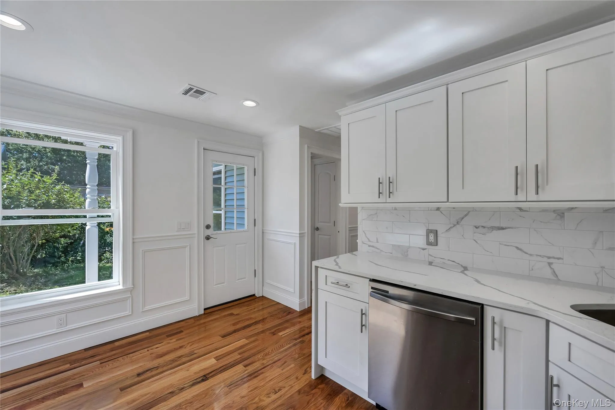 Kitchen with stainless steel dishwasher, light stone countertops, white cabinetry, dark wood-style floors, and recessed lighting Kitchen with stainless steel dishwasher, light stone countertops, white cabinetry, dark wood-style floors, and recessed lighting