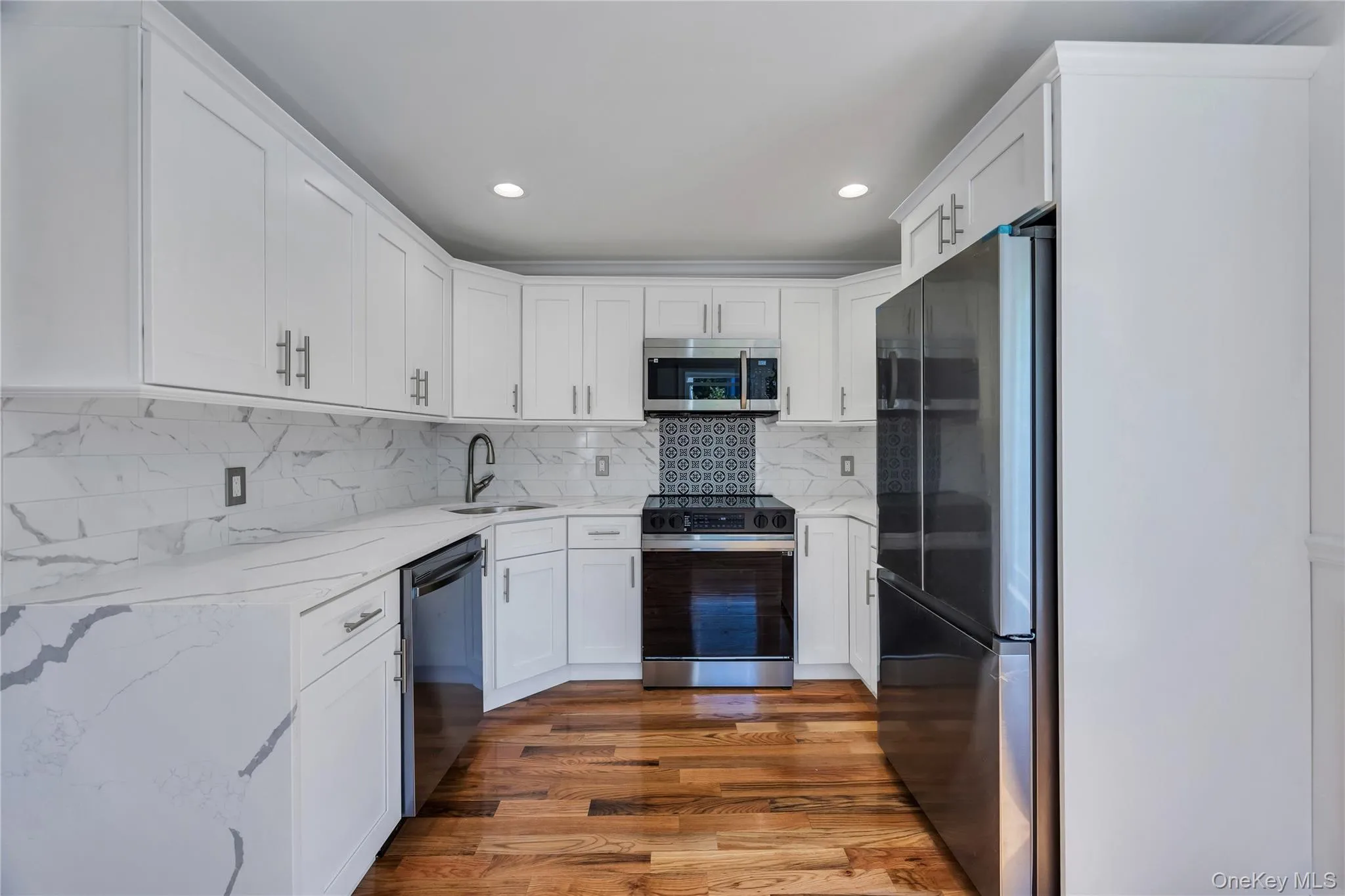 Kitchen featuring light stone counters, appliances with stainless steel finishes, dark wood-style flooring, white cabinetry, and recessed lighting Kitchen featuring light stone counters, appliances with stainless steel finishes, dark wood-style flooring, white cabinetry, and recessed lighting