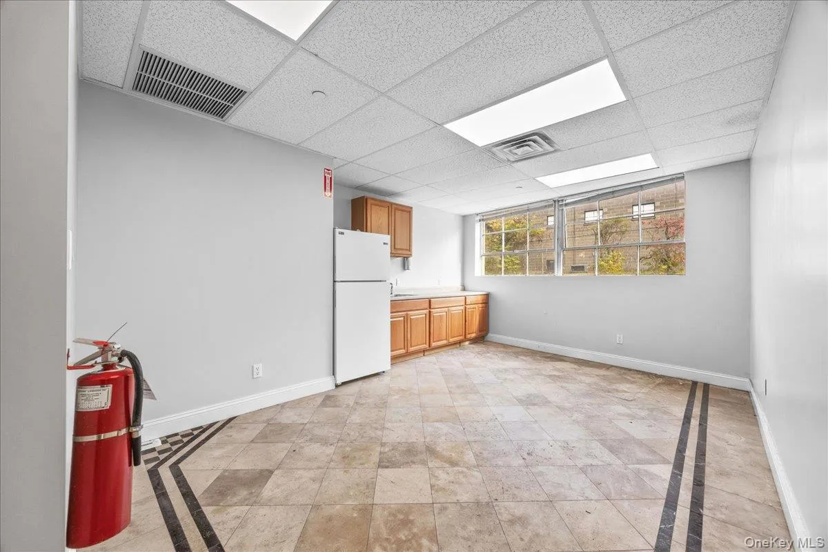 Kitchen with a paneled ceiling, light countertops, freestanding refrigerator, inlaid floor details, and brown cabinetry Kitchen with a paneled ceiling, light countertops, freestanding refrigerator, inlaid floor details, and brown cabinetry