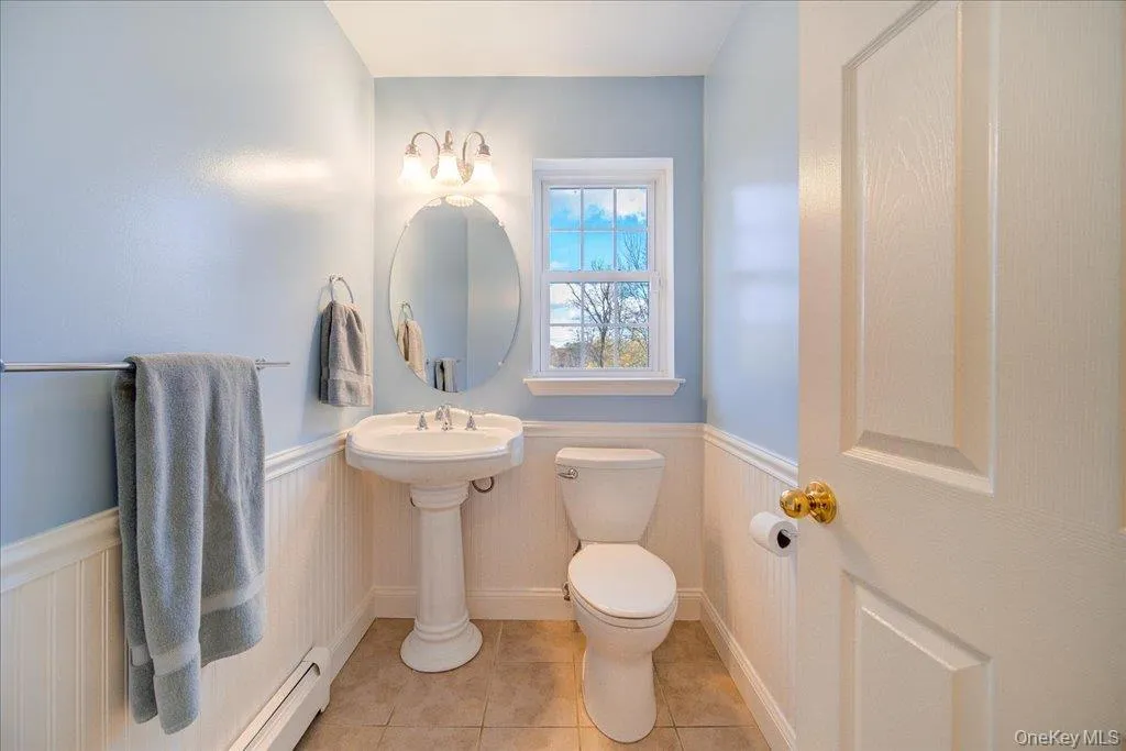1/2 Bathroom with baseboard heating, a wainscoted wall, and light tile patterned flooring 1/2 Bathroom with baseboard heating, a wainscoted wall, and light tile patterned flooring