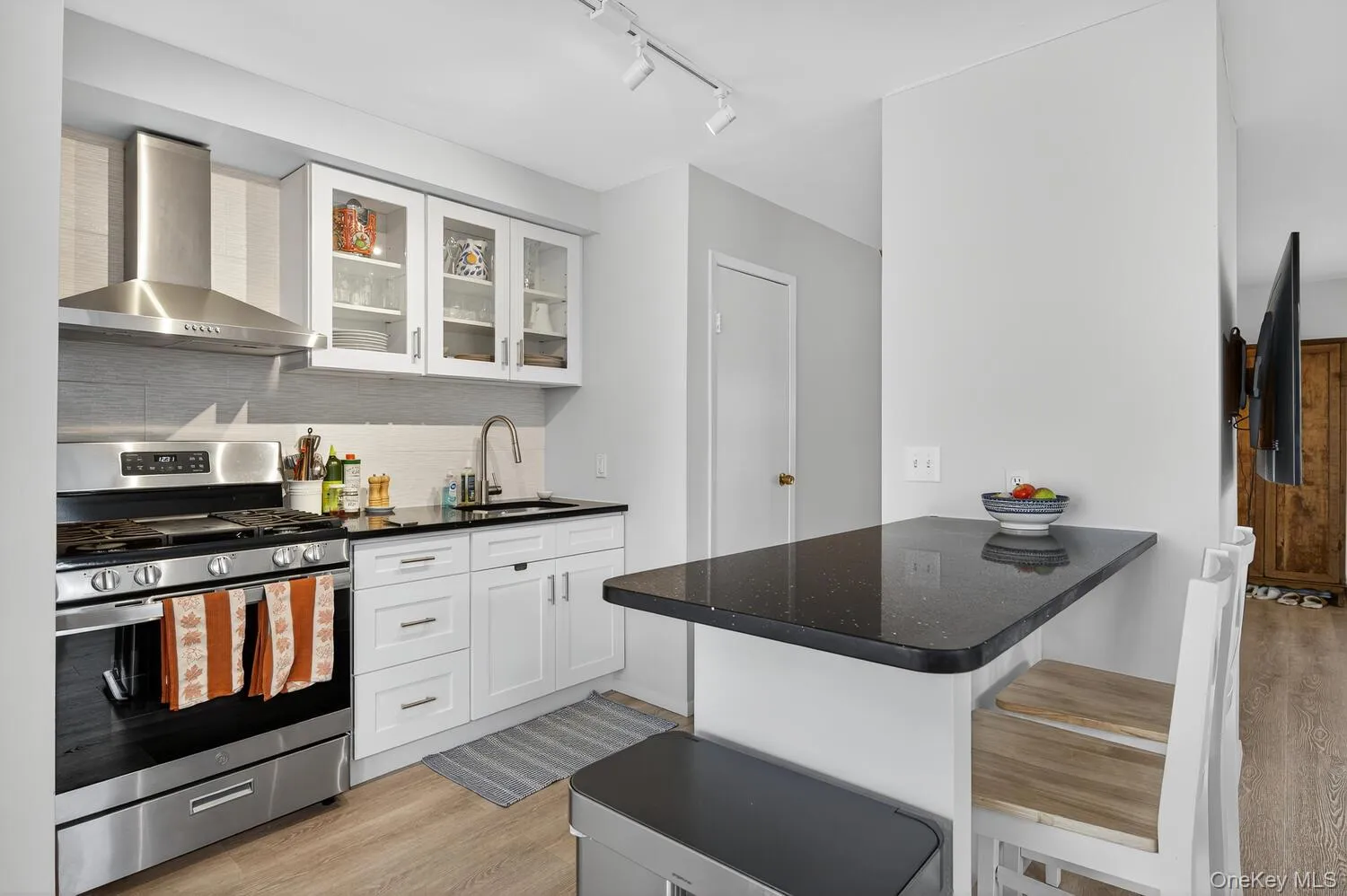 Kitchen featuring gas range, wall chimney range hood, light wood-style flooring, backsplash, and a breakfast bar Kitchen featuring gas range, wall chimney range hood, light wood-style flooring, backsplash, and a breakfast bar