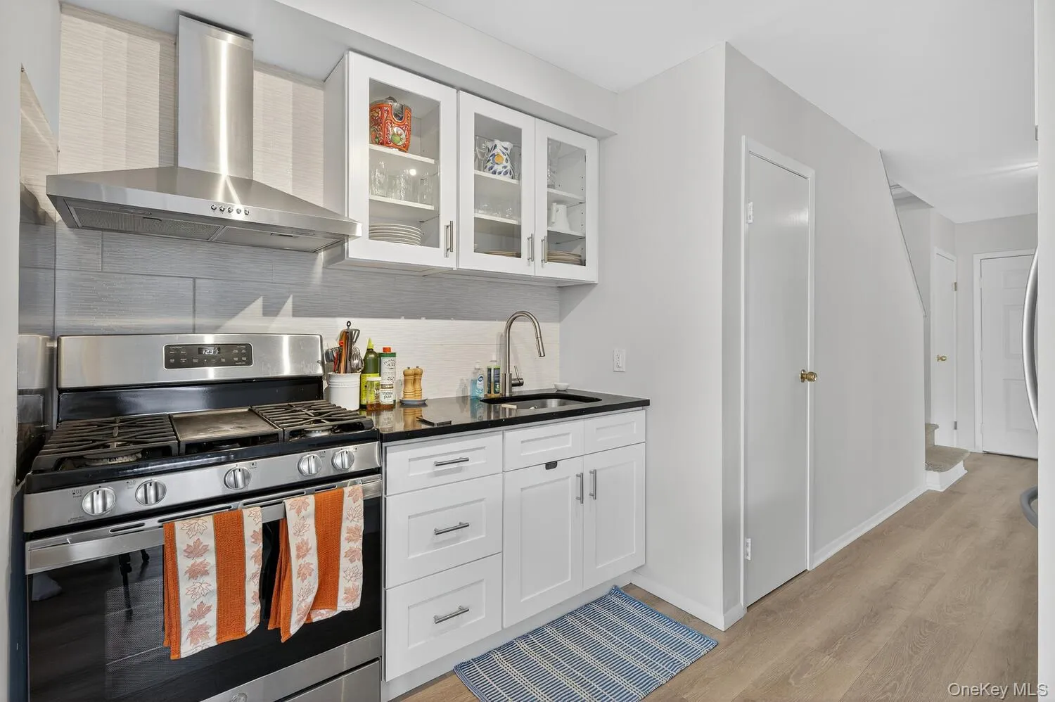 Kitchen featuring gas stove, wall chimney exhaust hood, tasteful backsplash, glass insert cabinets, and white cabinets Kitchen featuring gas stove, wall chimney exhaust hood, tasteful backsplash, glass insert cabinets, and white cabinets