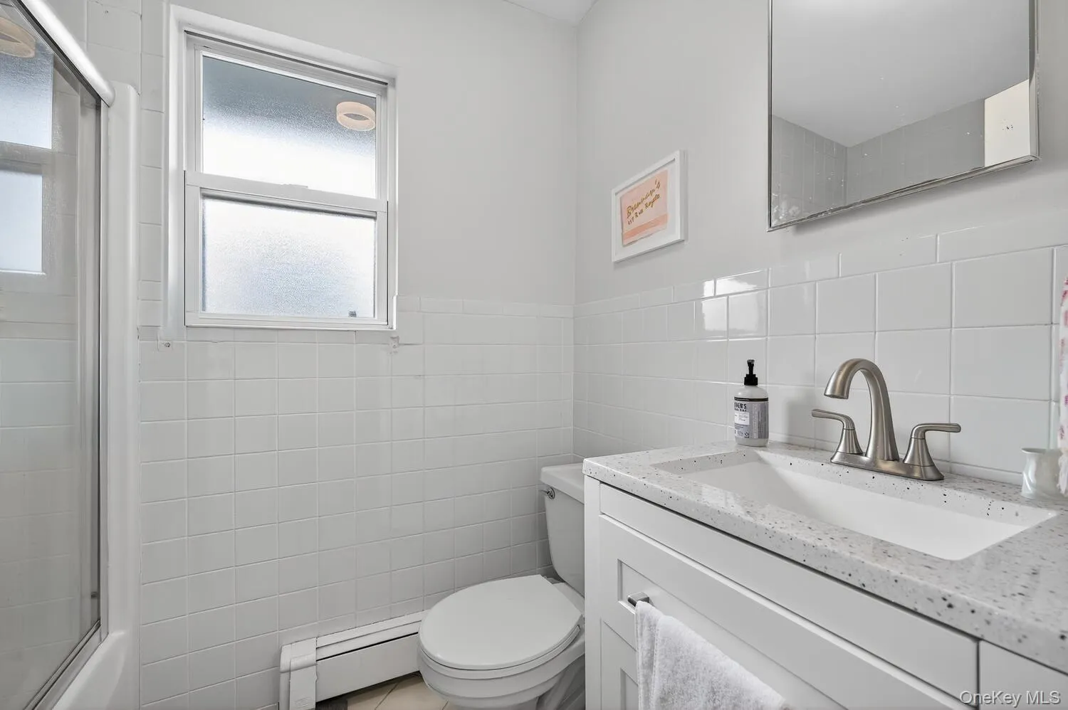 Bathroom with vanity, tile walls, a baseboard heating unit, bath / shower combo with glass door, and a wainscoted wall Bathroom with vanity, tile walls, a baseboard heating unit, bath / shower combo with glass door, and a wainscoted wall