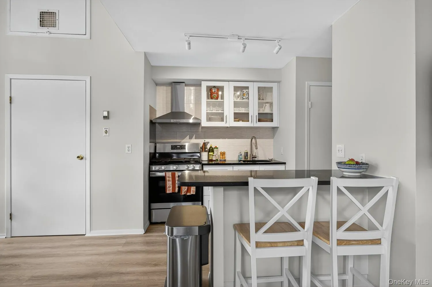 Kitchen featuring a breakfast bar area, stainless steel gas stove, wall chimney exhaust hood, tasteful backsplash, and a peninsula Kitchen featuring a breakfast bar area, stainless steel gas stove, wall chimney exhaust hood, tasteful backsplash, and a peninsula