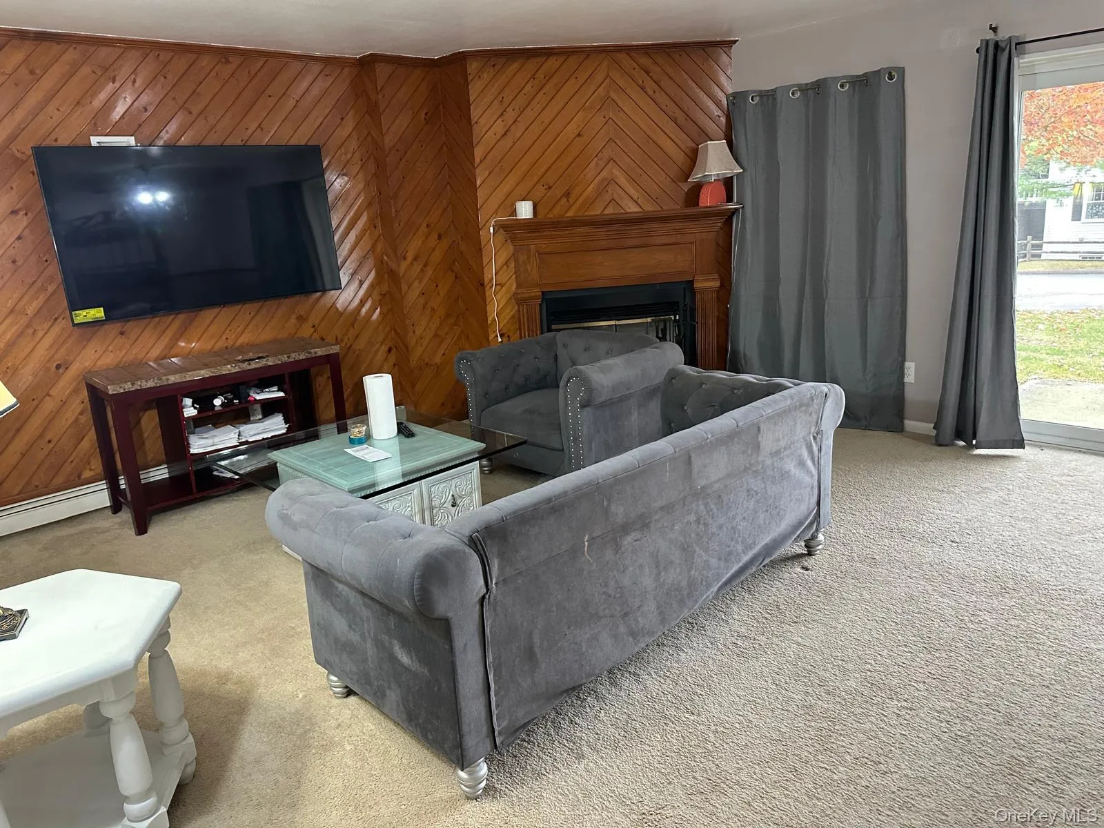 Living room featuring wooden walls, carpet flooring, and a fireplace Living room featuring wooden walls, carpet flooring, and a fireplace