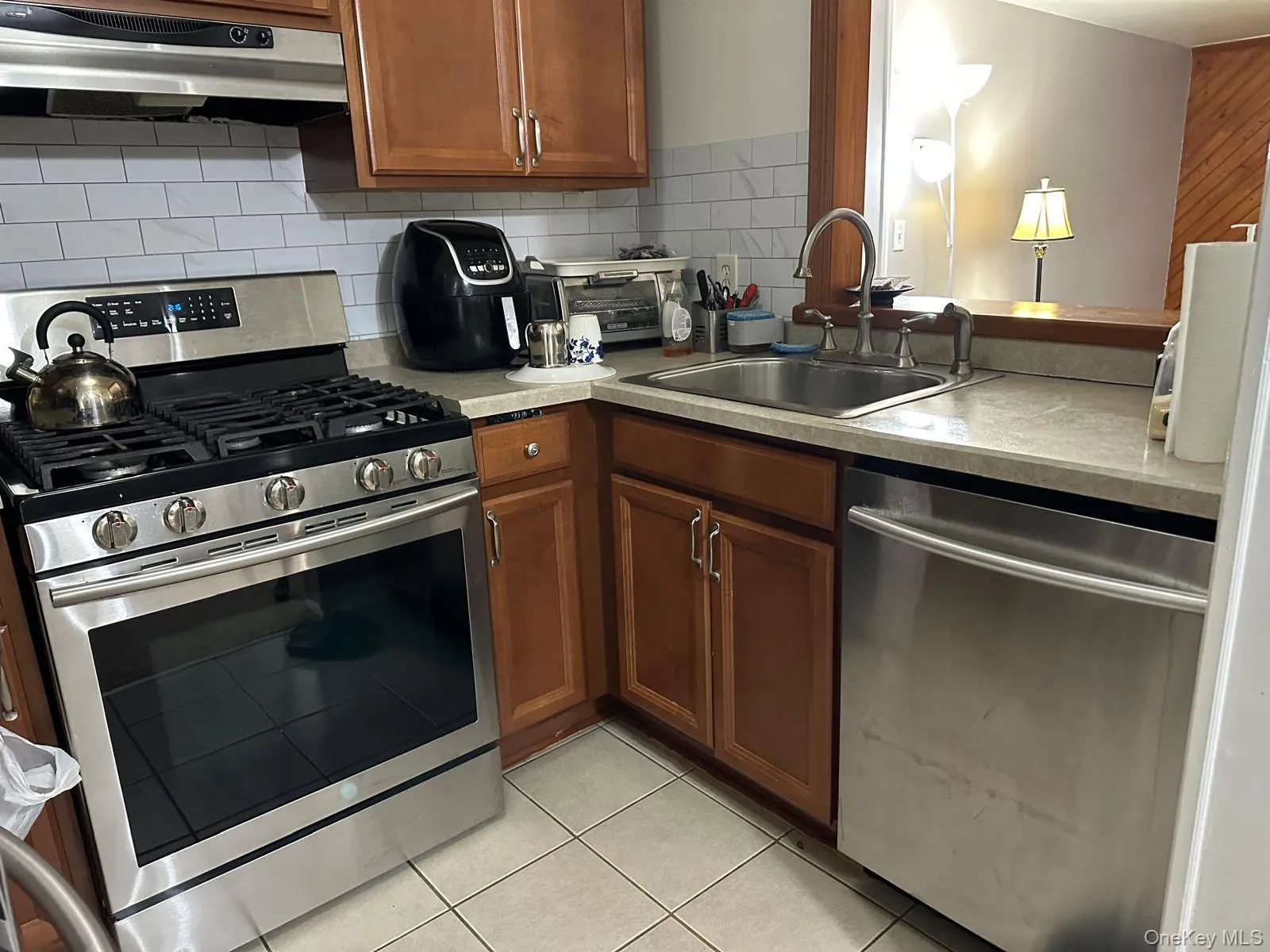 Kitchen with stainless steel appliances, under cabinet range hood, brown cabinetry, backsplash, and light tile patterned floors Kitchen with stainless steel appliances, under cabinet range hood, brown cabinetry, backsplash, and light tile patterned floors