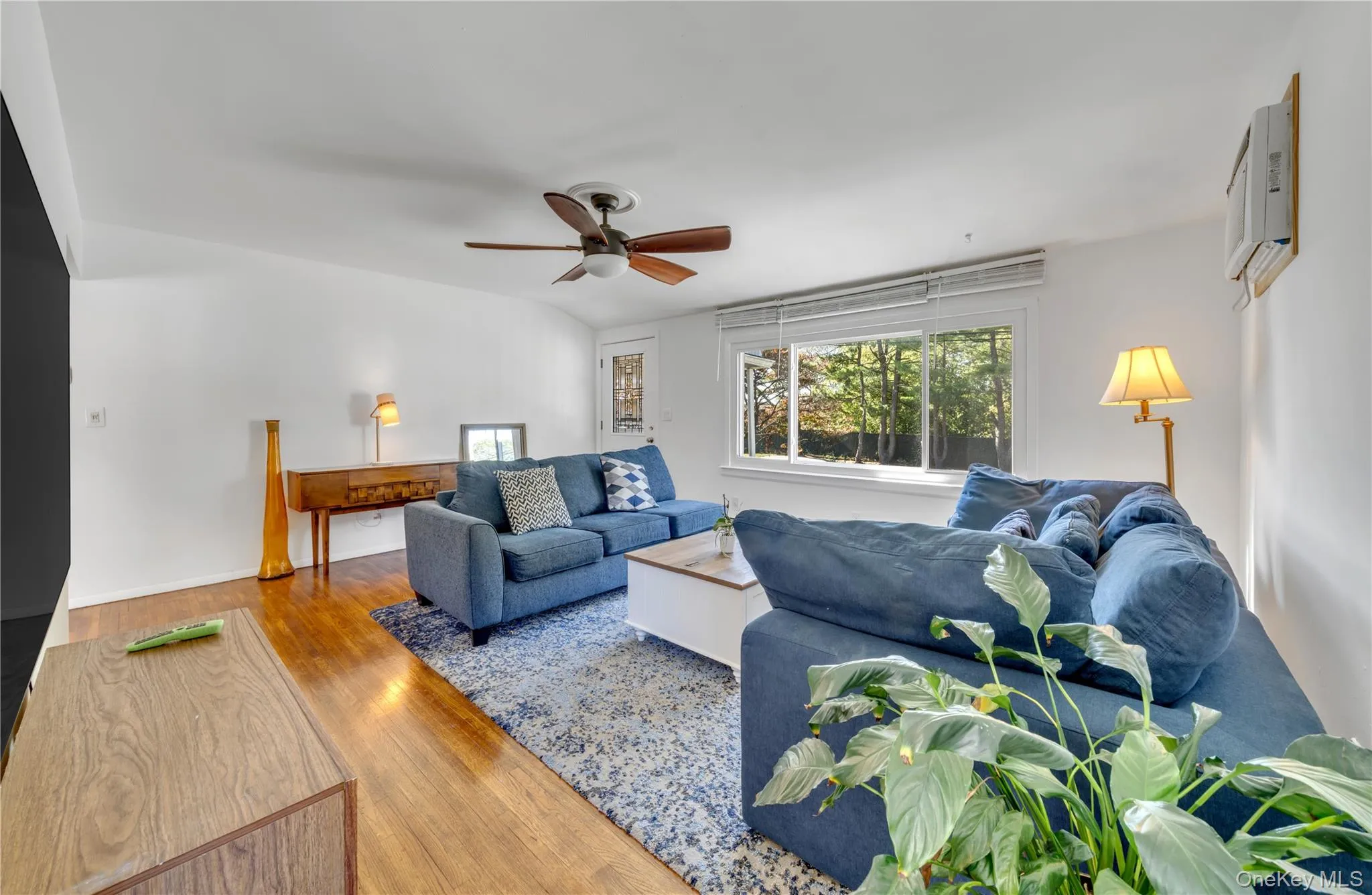 Living room featuring wood finished floors, ceiling fan, and a wall mounted air conditioner Living room featuring wood finished floors, ceiling fan, and a wall mounted air conditioner