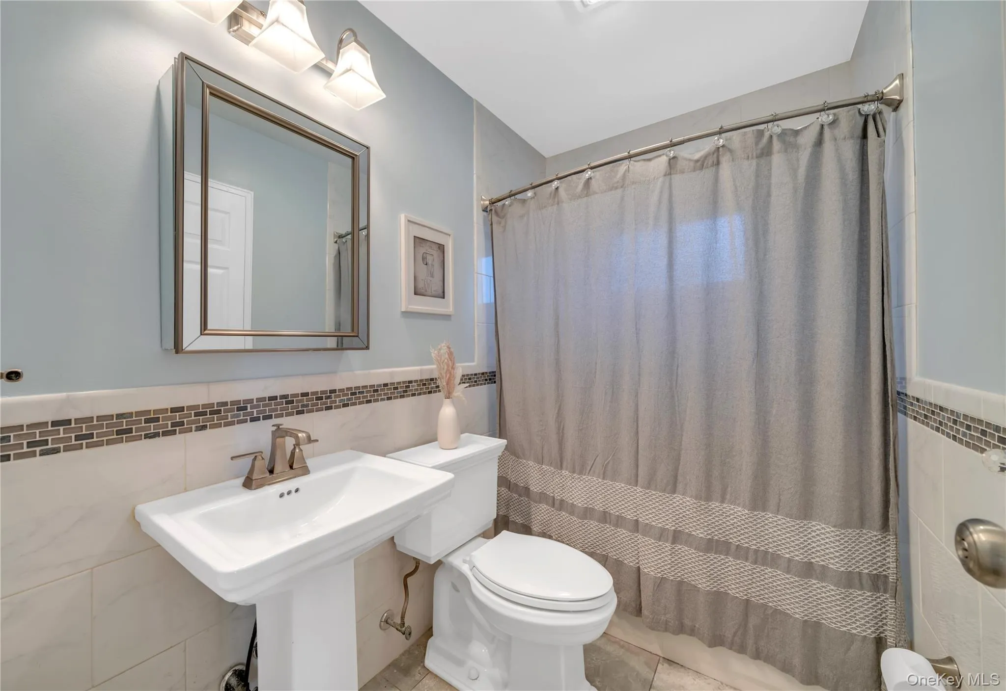 Full bathroom featuring tile walls, a wainscoted wall, and curtained shower Full bathroom featuring tile walls, a wainscoted wall, and curtained shower