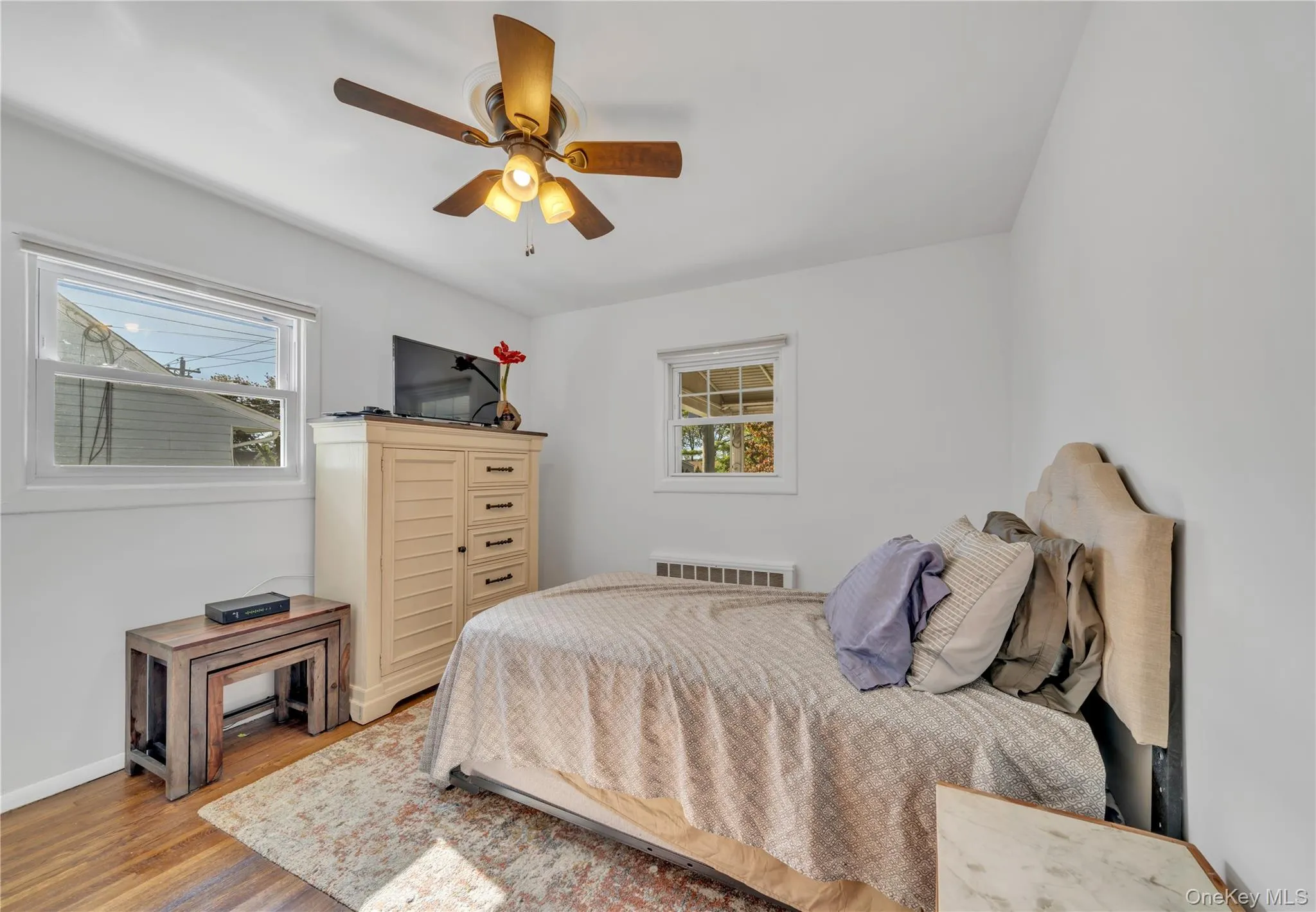 Bedroom with multiple windows, wood finished floors, ceiling fan, and radiator Bedroom with multiple windows, wood finished floors, ceiling fan, and radiator