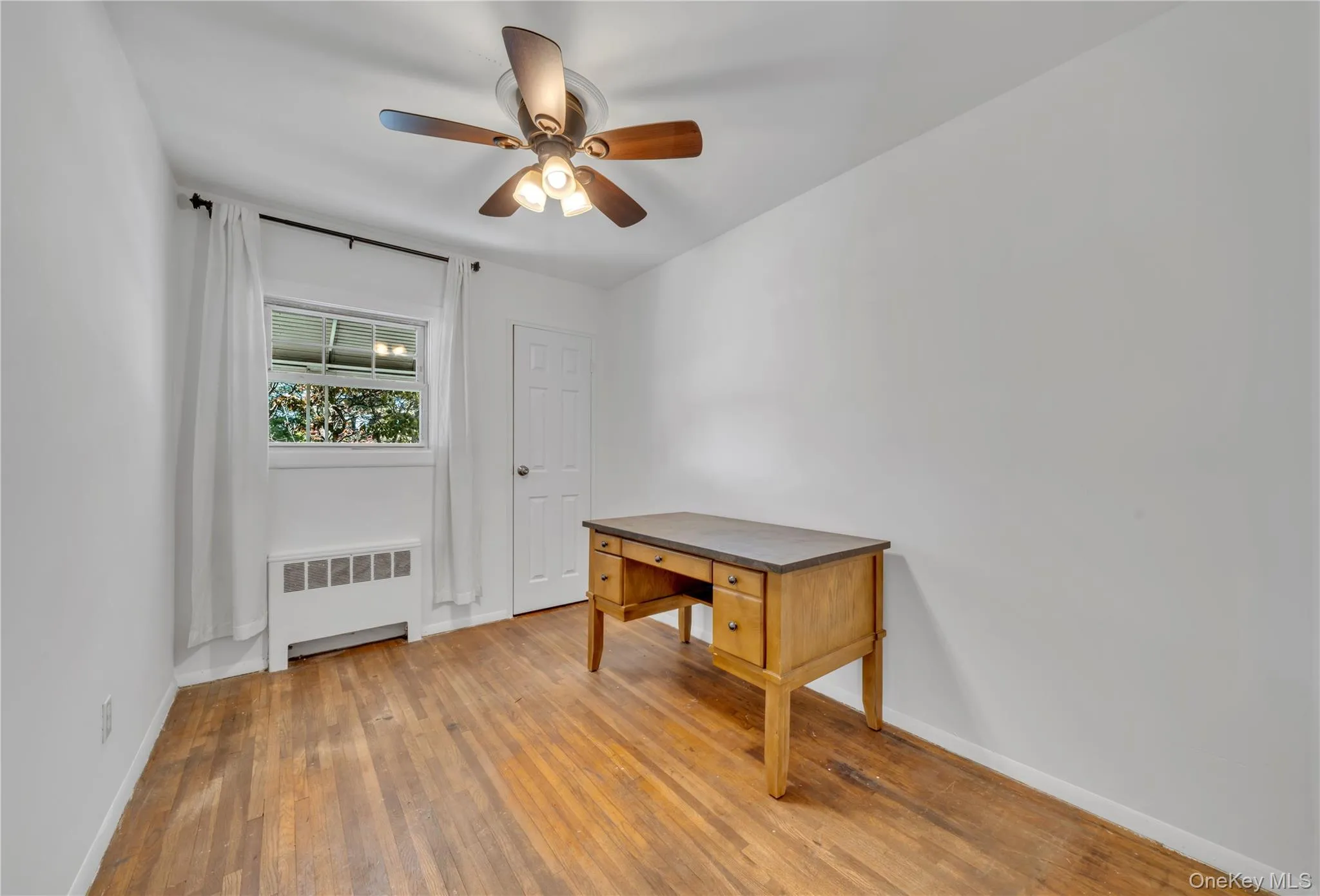 Unfurnished office featuring radiator, light wood-style floors, and ceiling fan Unfurnished office featuring radiator, light wood-style floors, and ceiling fan